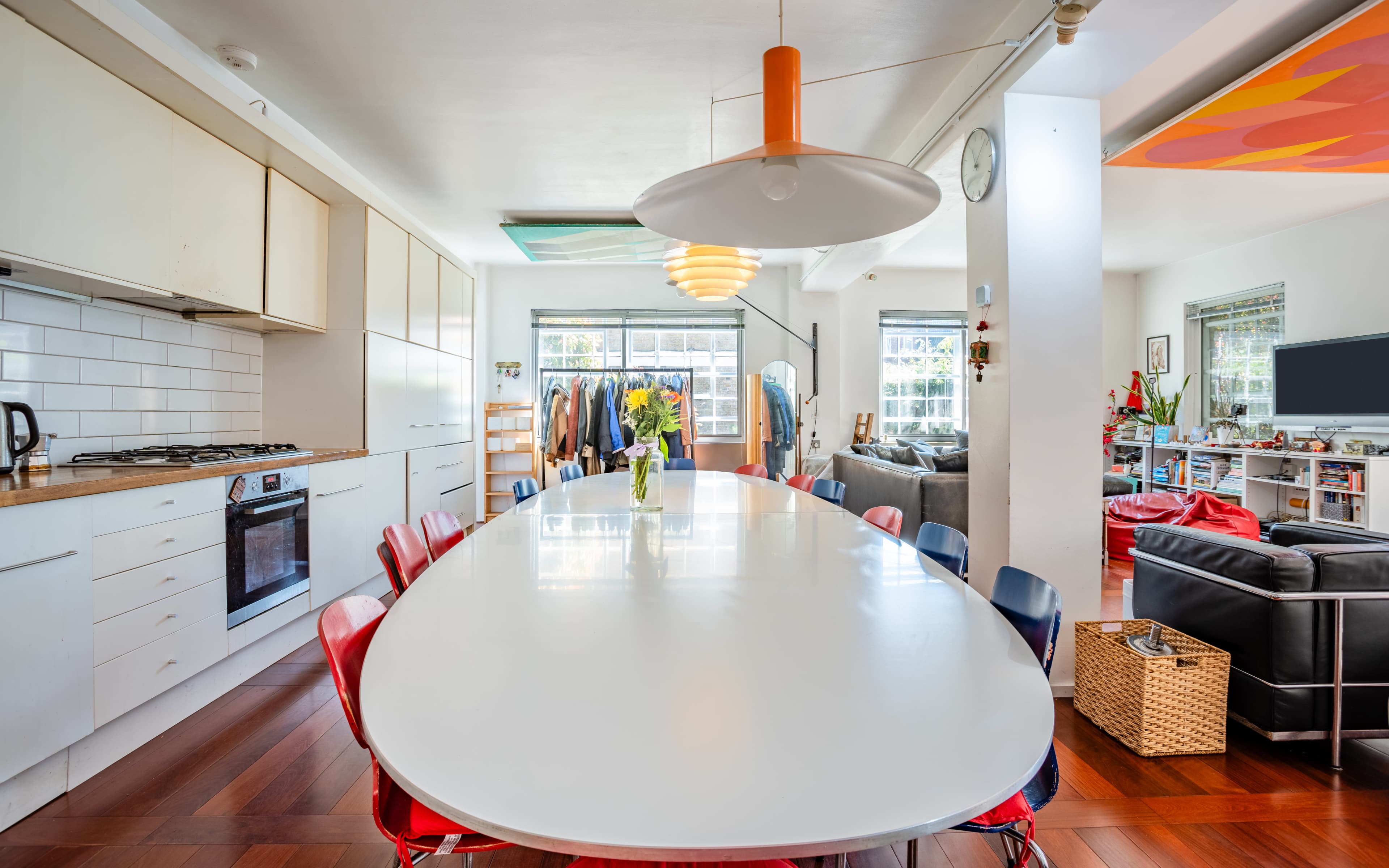 A modern kitchen and dining area features a large white table surrounded by colorful chairs, with natural light streaming through windows.
