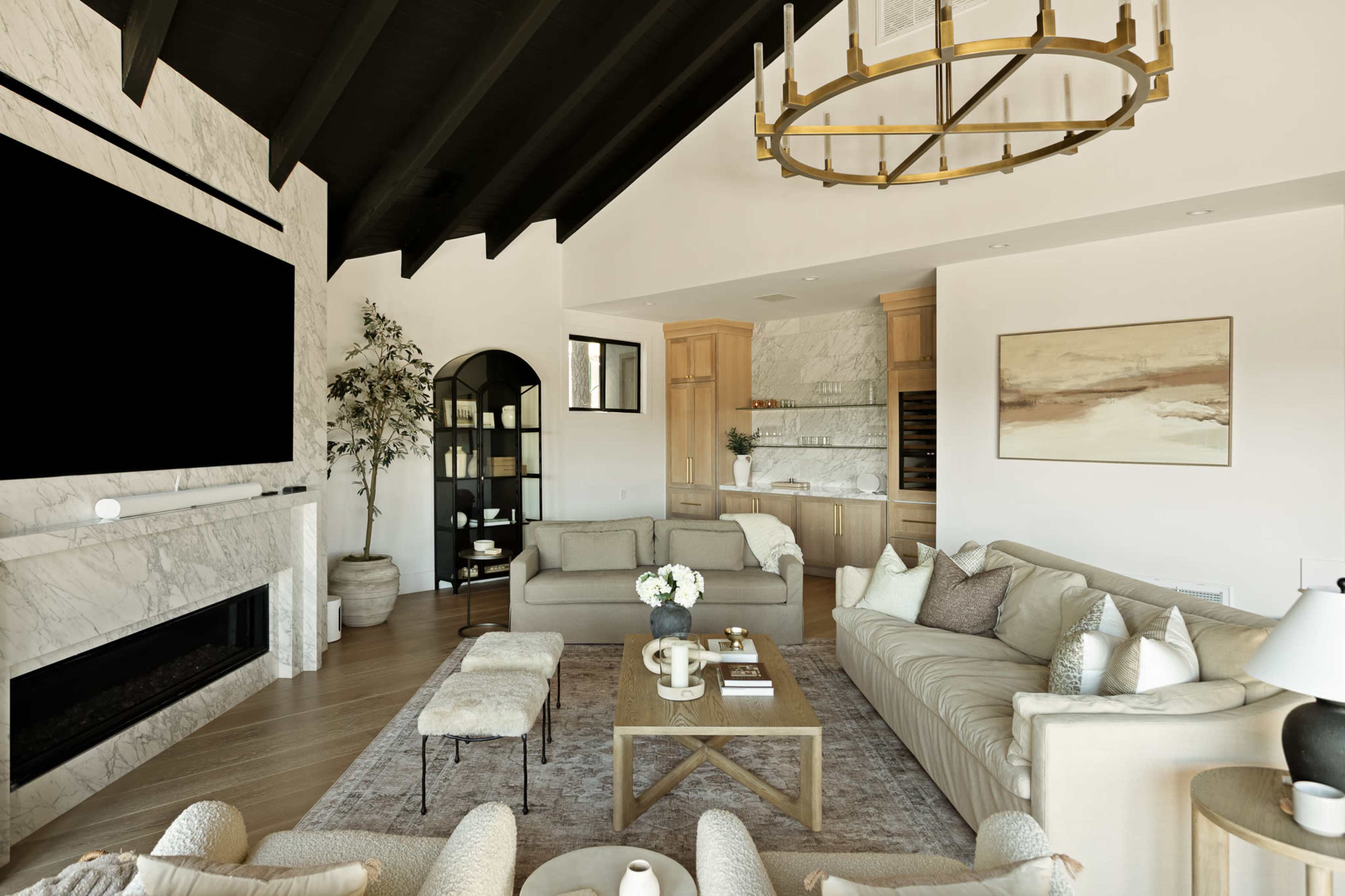 The image shows a modern living room with a high ceiling, featuring marble accents, a large television area, and an arrangement of comfortable sofas around a coffee table.