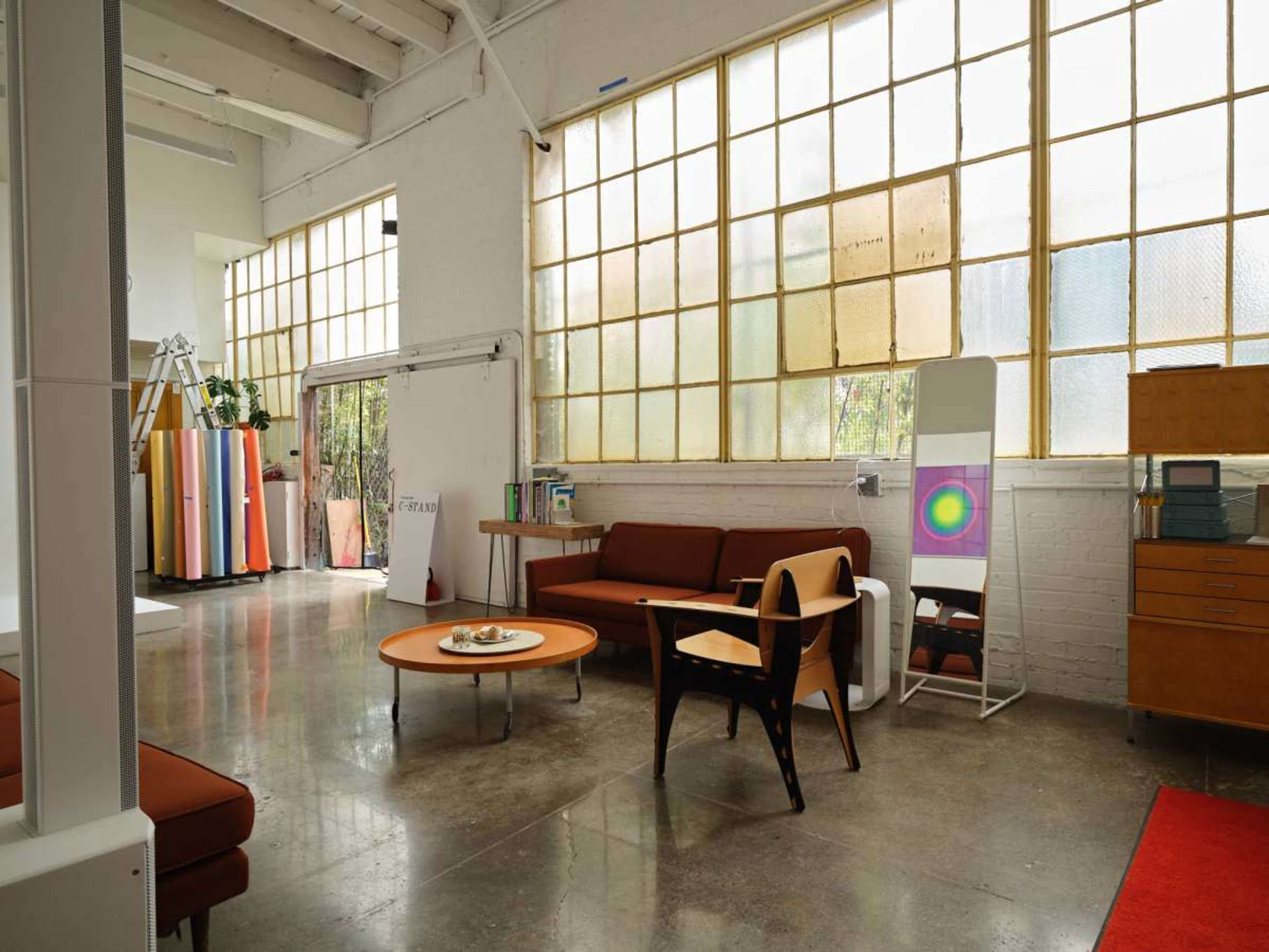 The image depicts a modern interior space featuring large windows, minimalist furniture, and a polished concrete floor.