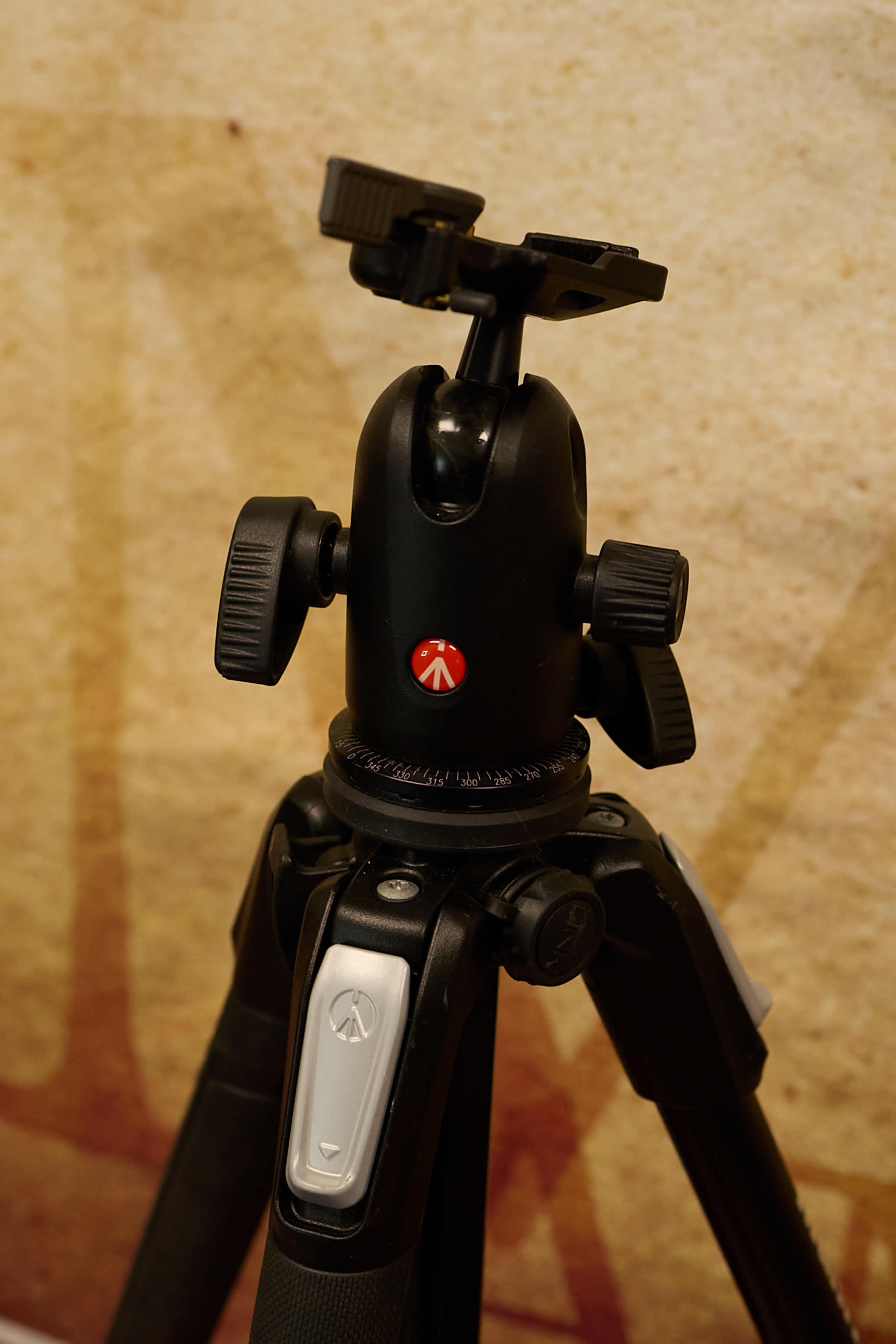 The image shows a black tripod head mounted on a tripod, featuring adjustment knobs and a quick-release plate.