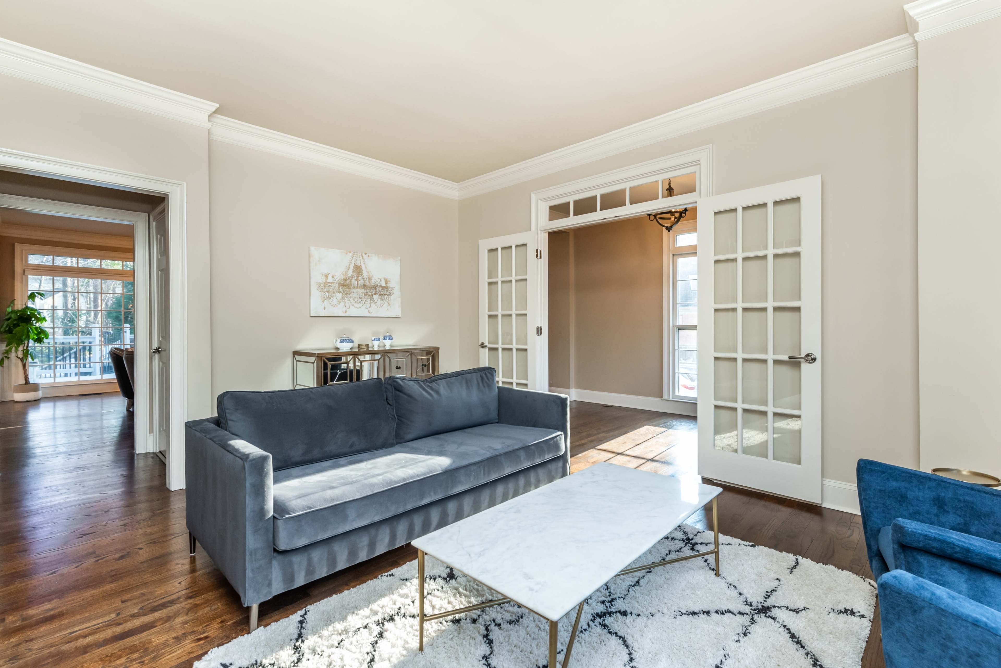 A living room features a gray sofa, a marble-top coffee table, and glass-paneled doors leading to another space.