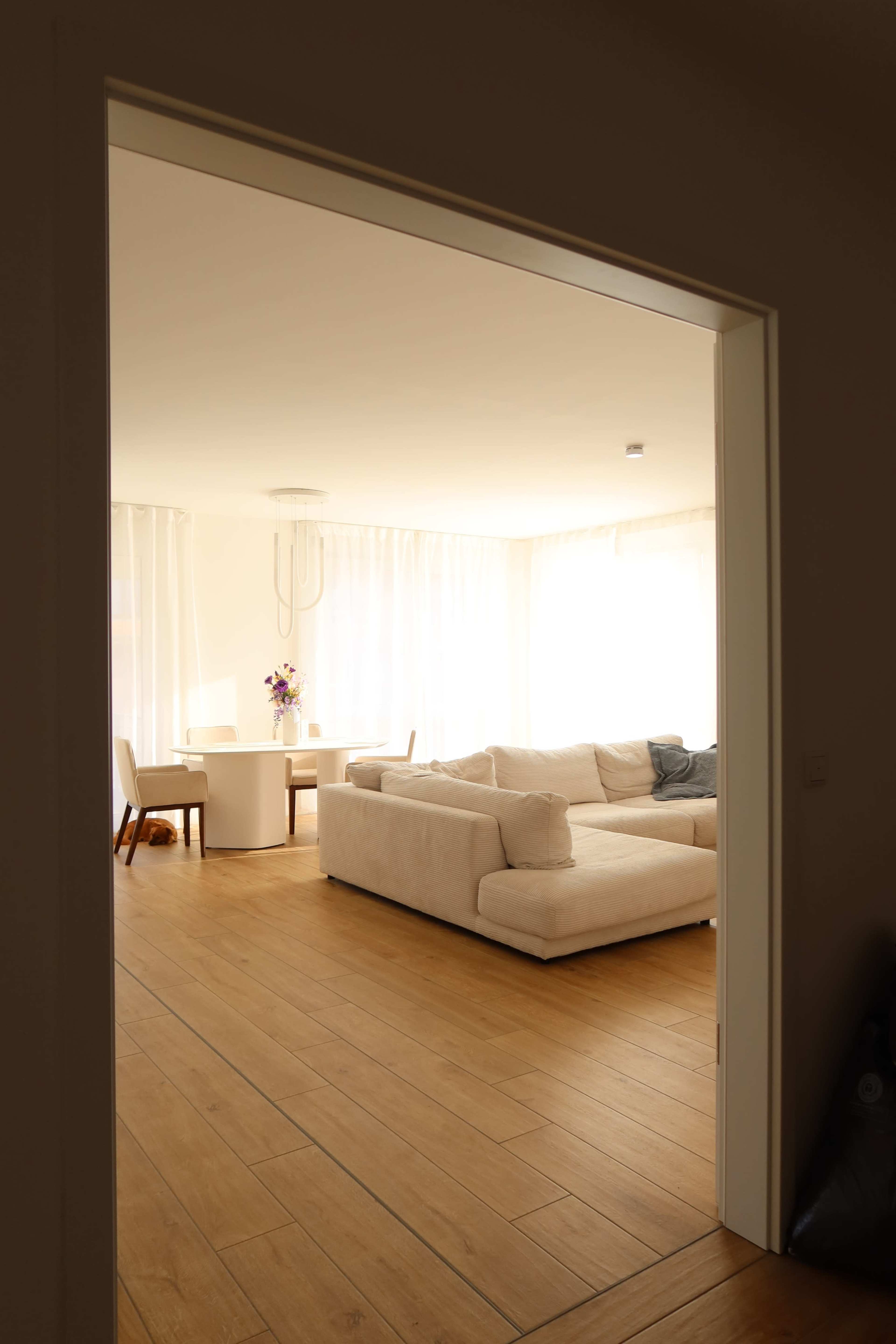 A well-lit living room with a white sofa and a dining table is visible through an open doorway.