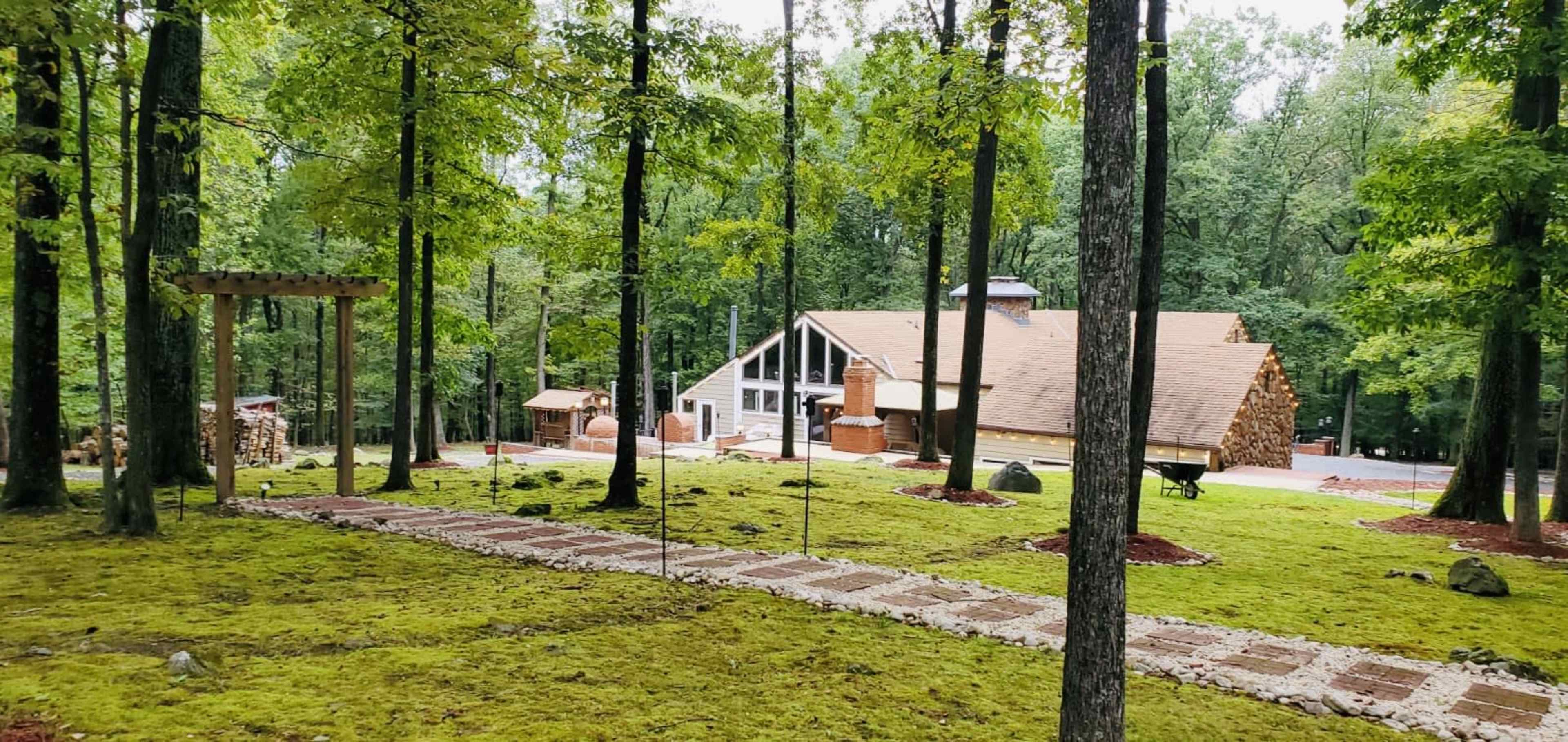 A spacious house is surrounded by trees, with a stone pathway leading to it through a grassy area.
