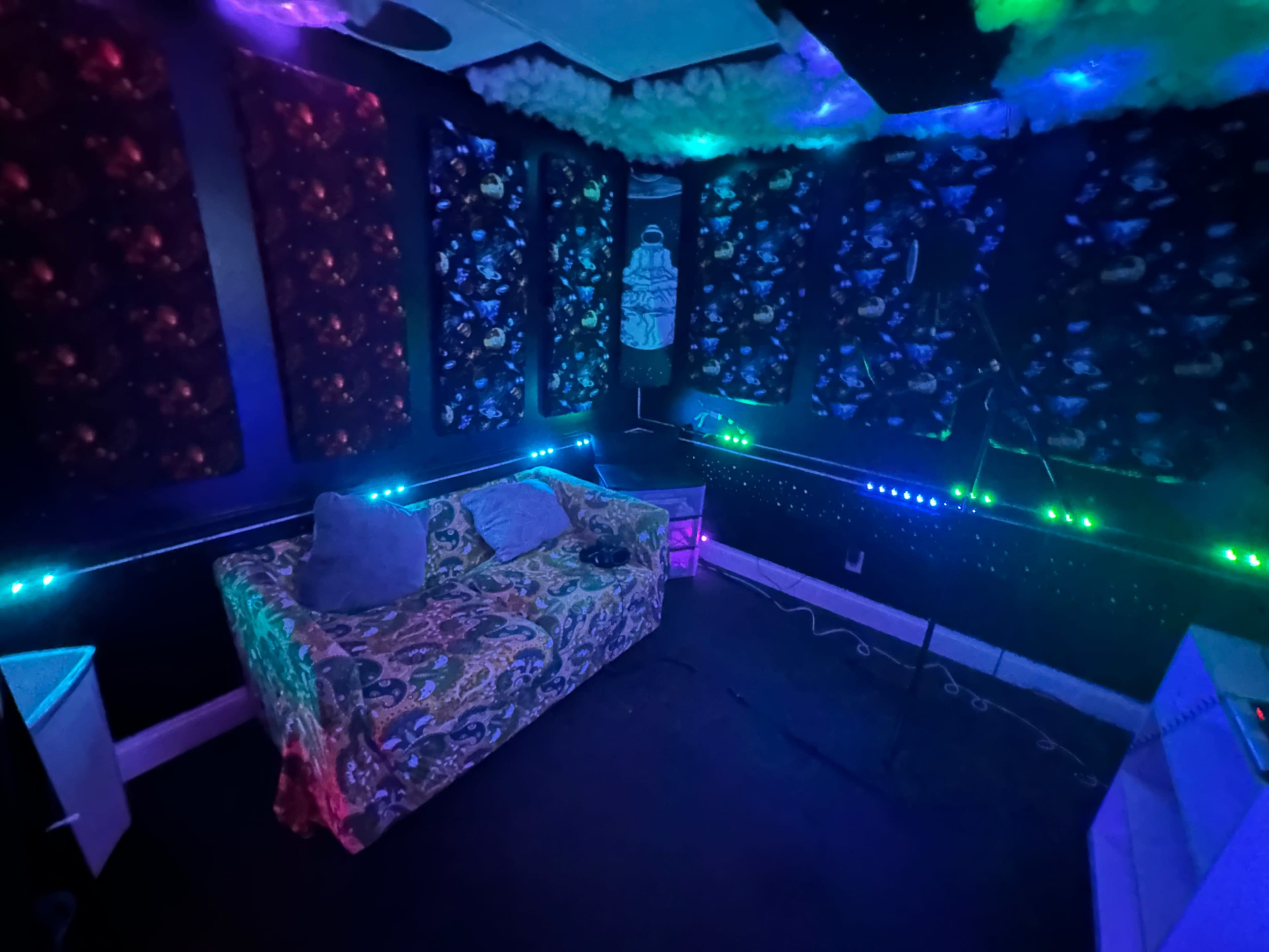 A dimly lit room with colorful LED lights, a patterned couch, and soundproofing panels on the walls.