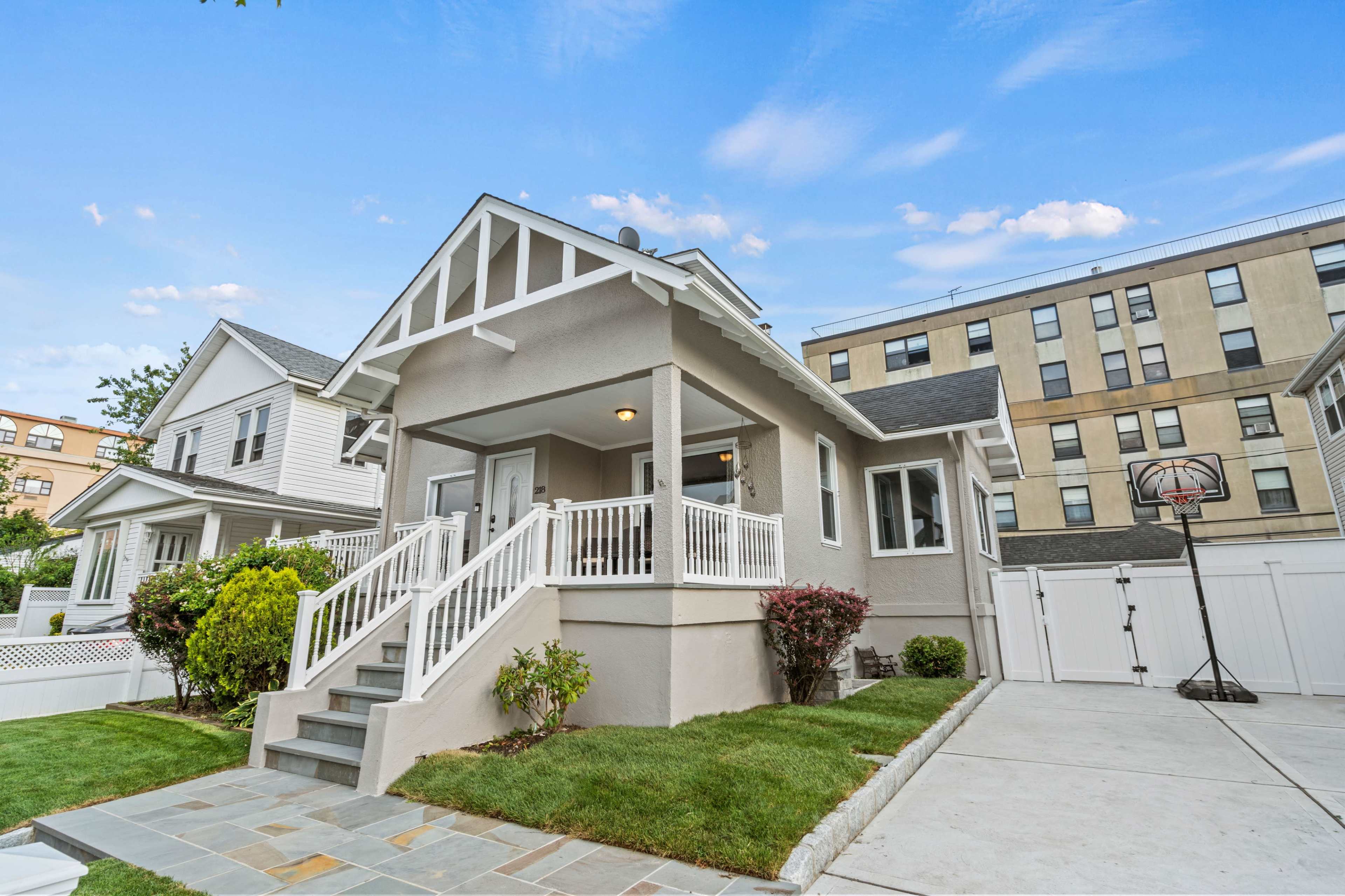 A single-family home with a front porch and stairs leads up to its entrance, surrounded by a well-maintained lawn and a basketball hoop nearby.
