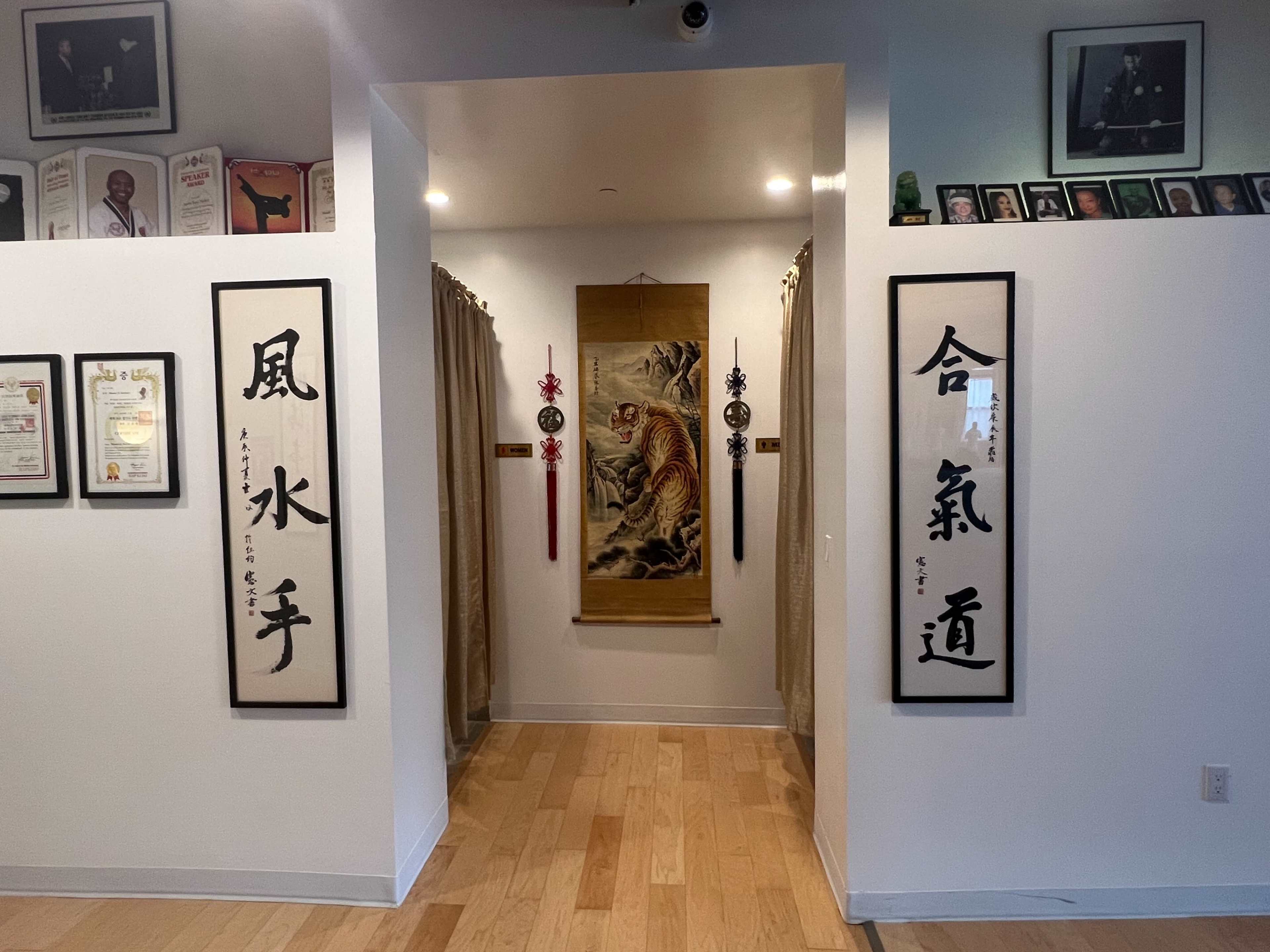 A hallway with framed certificates and photographs on the walls, flanked by curtains leading to a decorated space featuring a tiger-themed artwork.