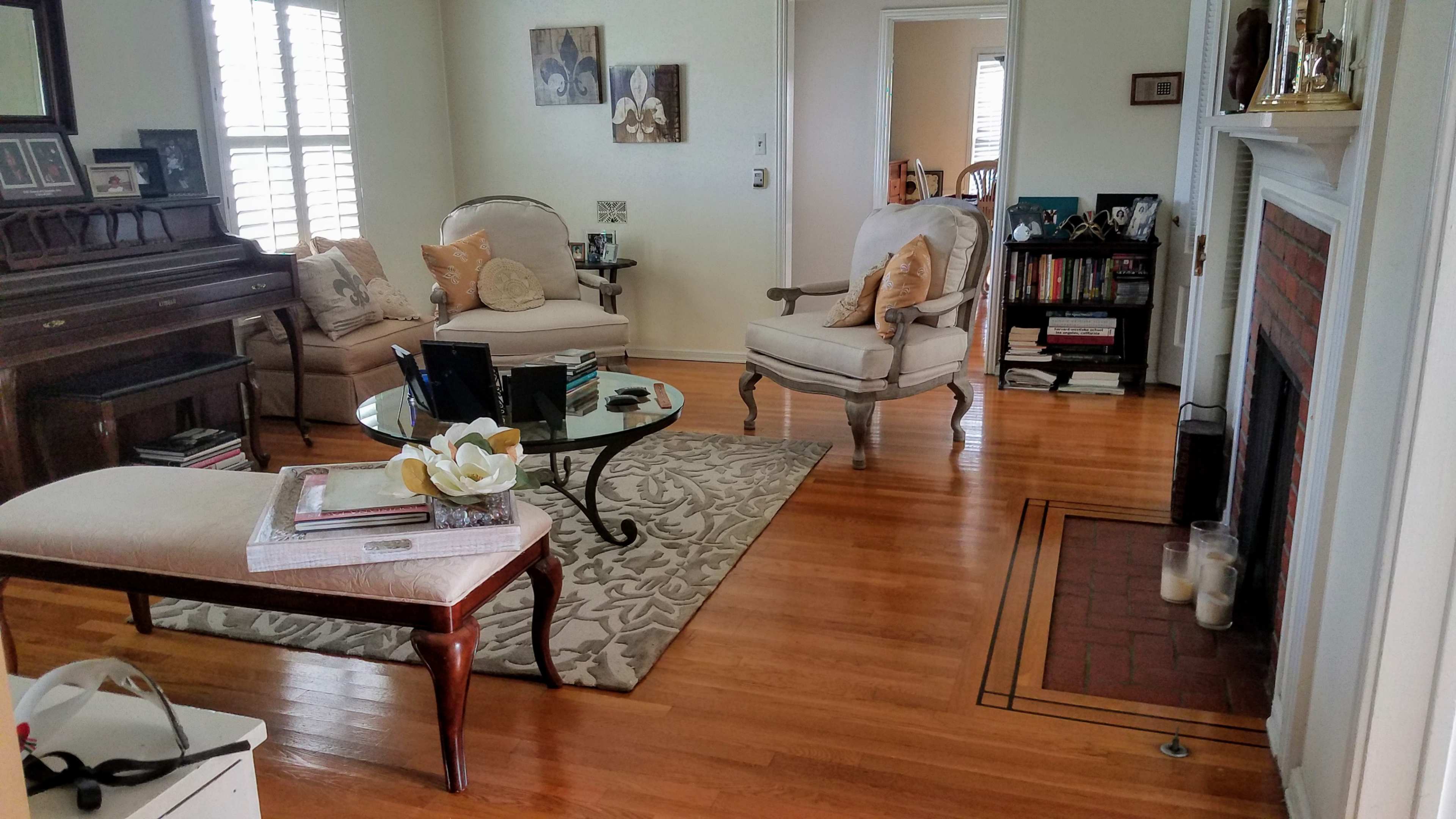 The image shows a living room with a piano, two armchairs, a coffee table, and a rug on wooden flooring.