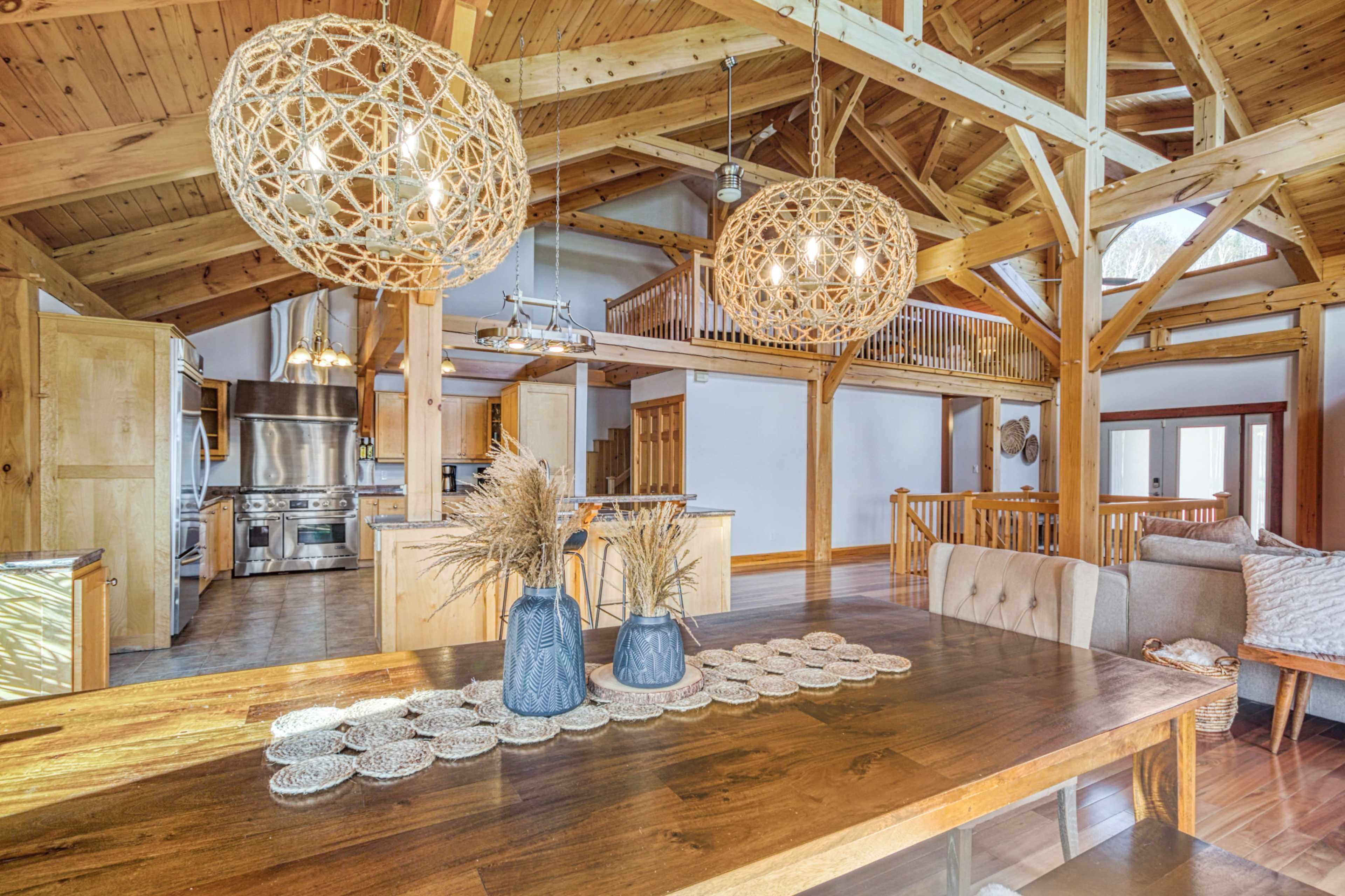 A spacious, rustic-style interior featuring wooden beams, large pendant lights, and a dining table set with decorative items.
