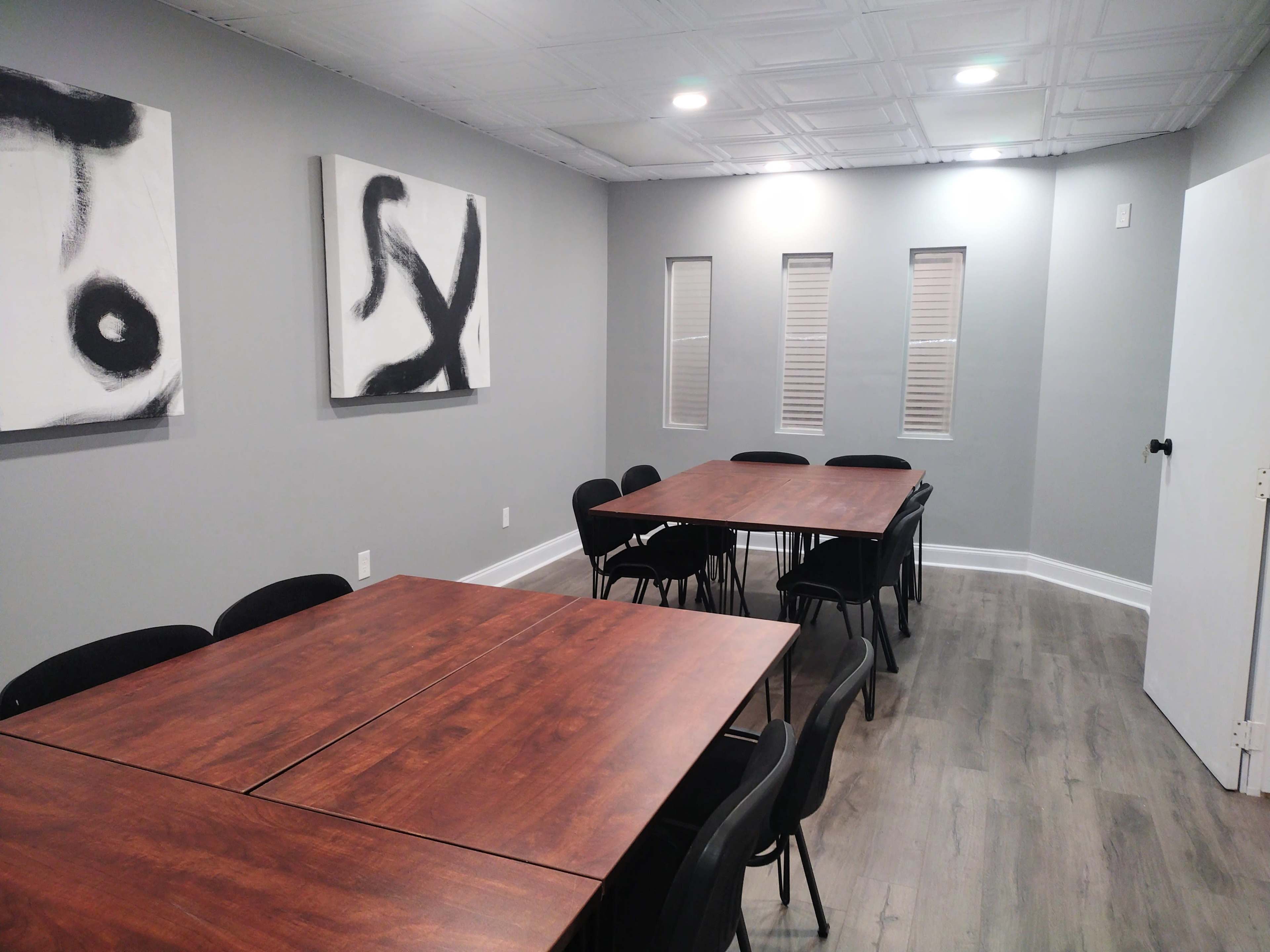 A meeting room with four wooden tables arranged in rows and black chairs, featuring abstract black-and-white artwork on the walls.
