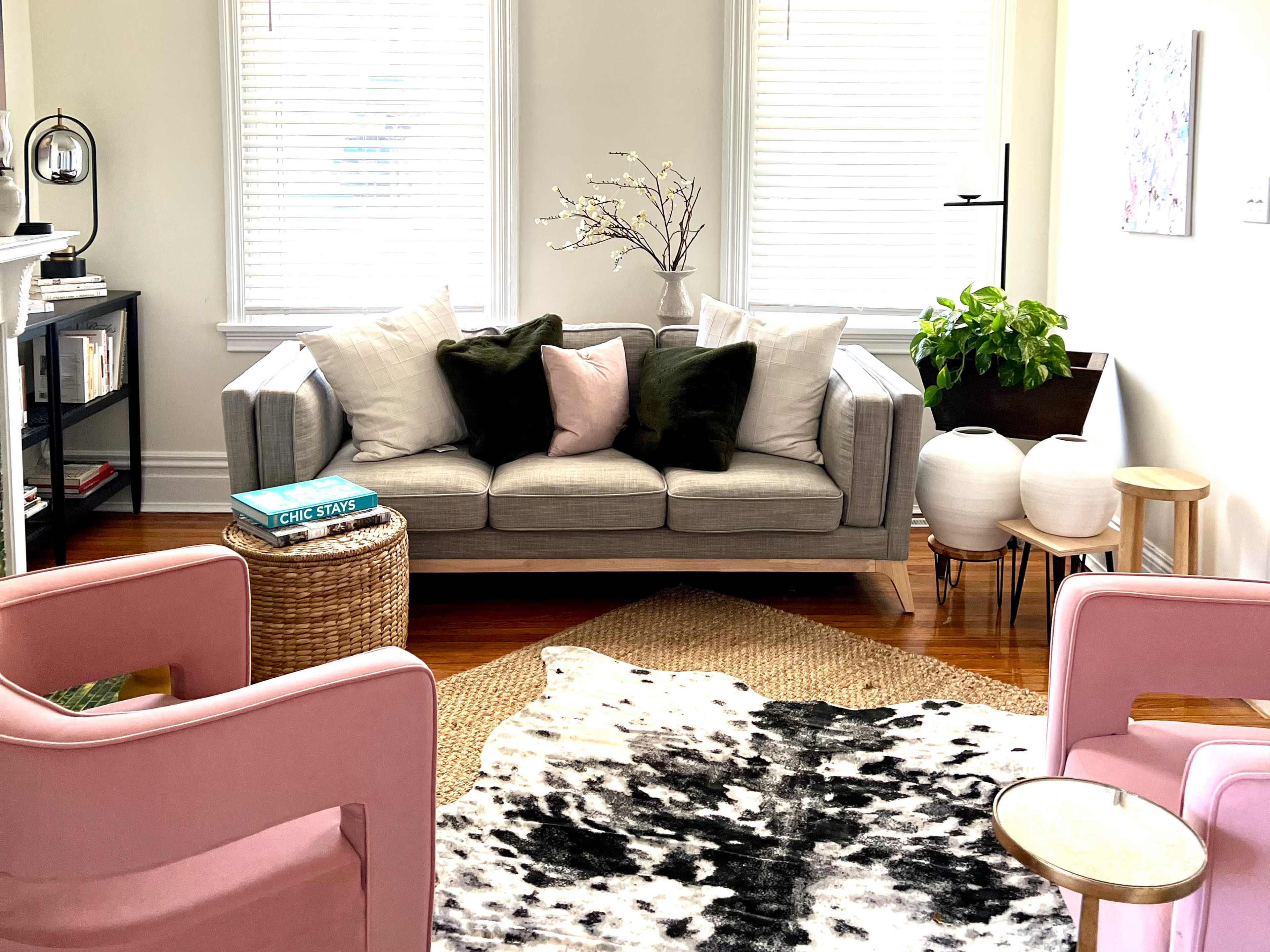 The living room features a gray sofa with pillows, two pink chairs, a cowhide rug, and indoor plants.