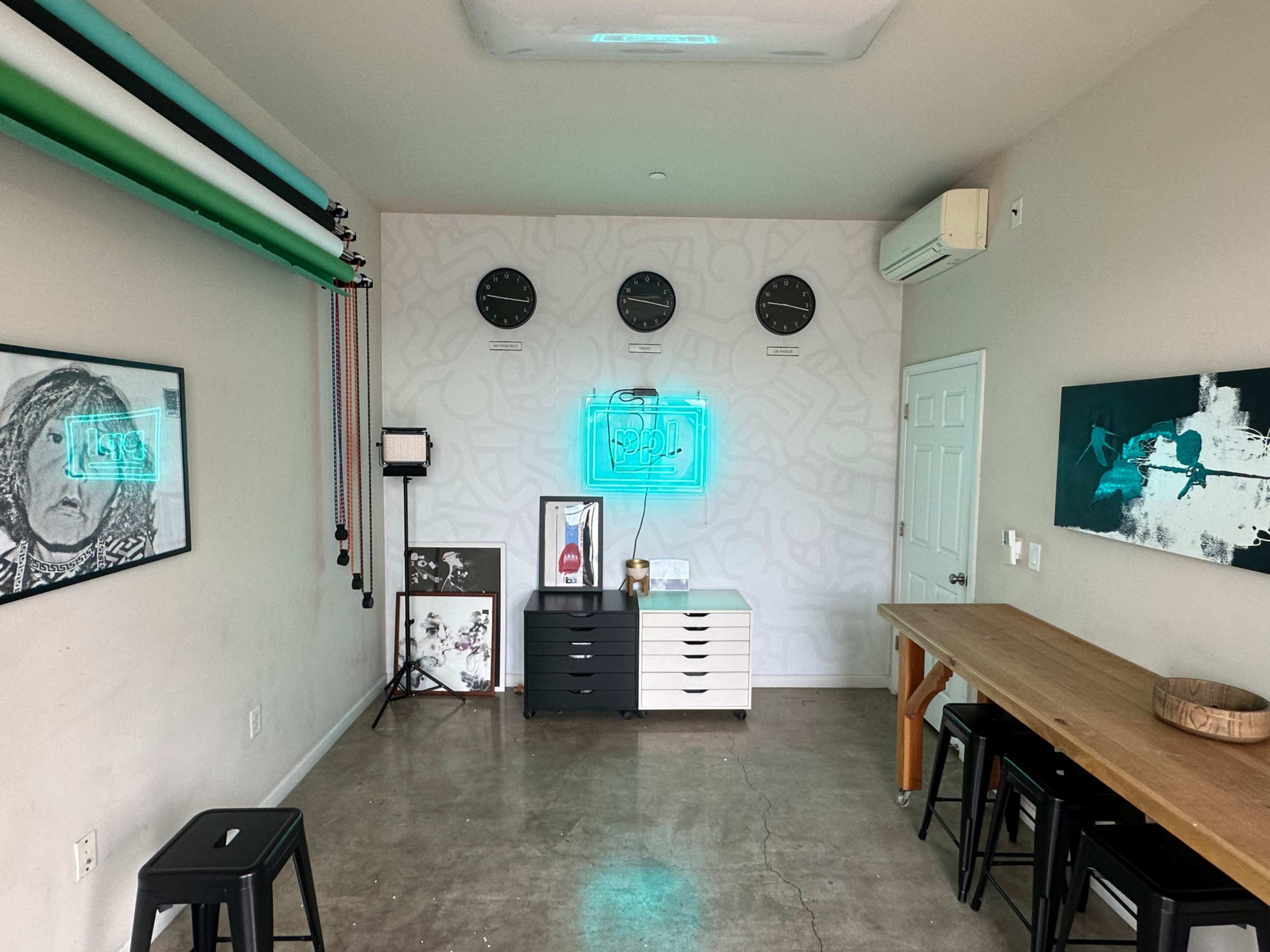 A modern studio or workspace featuring a large table, art on the walls, multiple clocks, and a color backdrop setup.