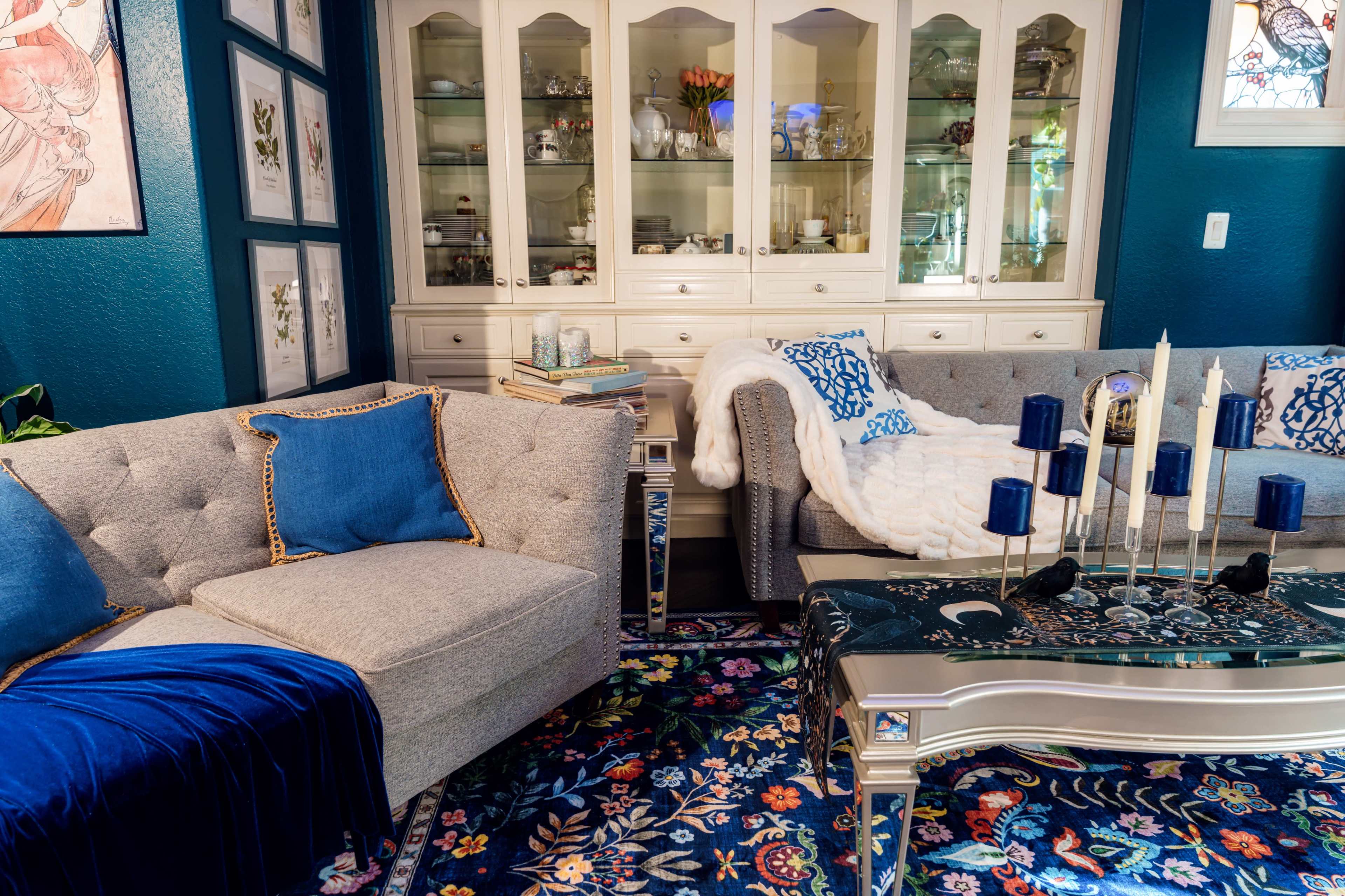 The image shows a cozy living room featuring two couches, a decorative coffee table with candles, and an array of framed artwork on the walls.