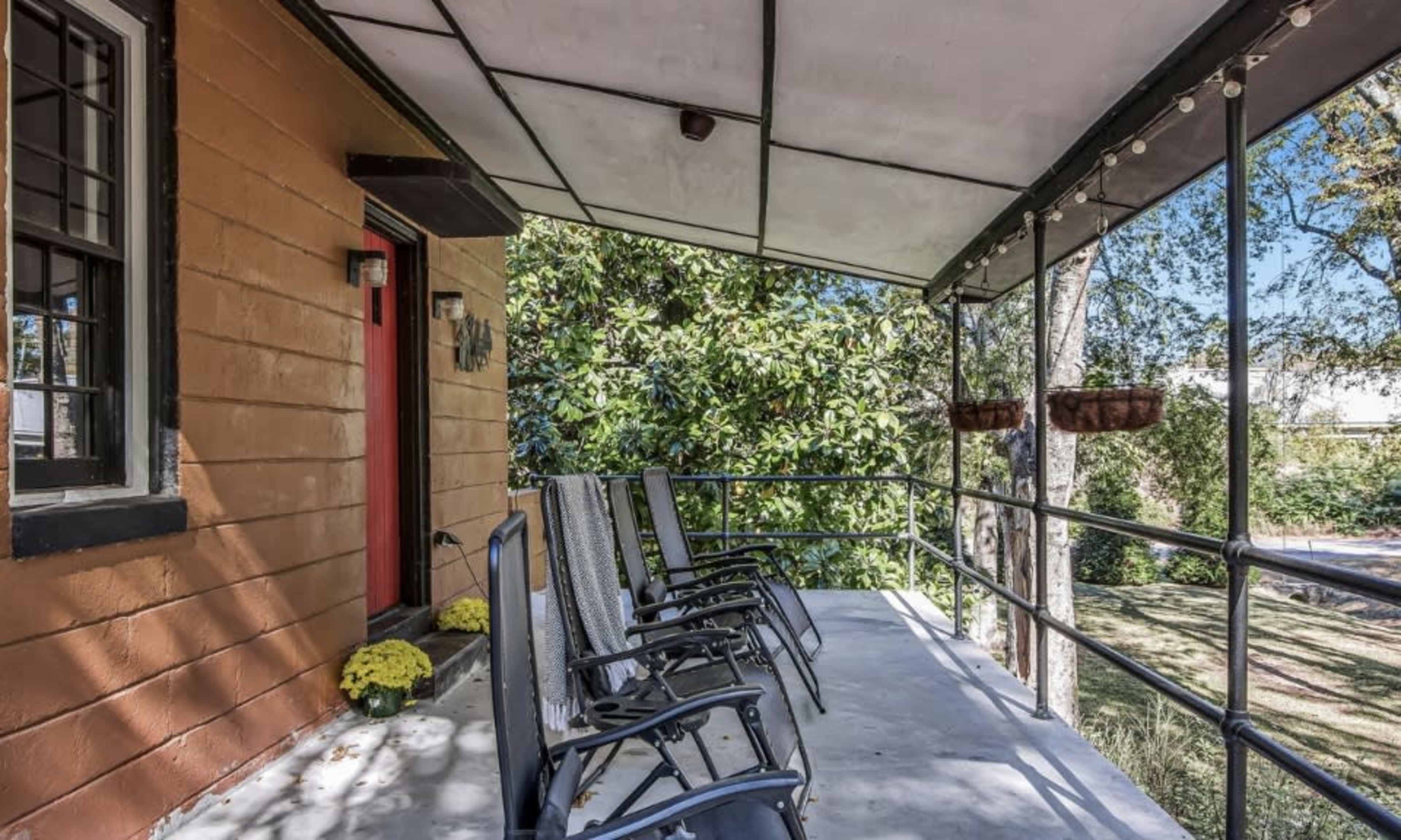 A covered porch with several black chairs arranged along a railing, surrounded by greenery and adorned with potted plants.