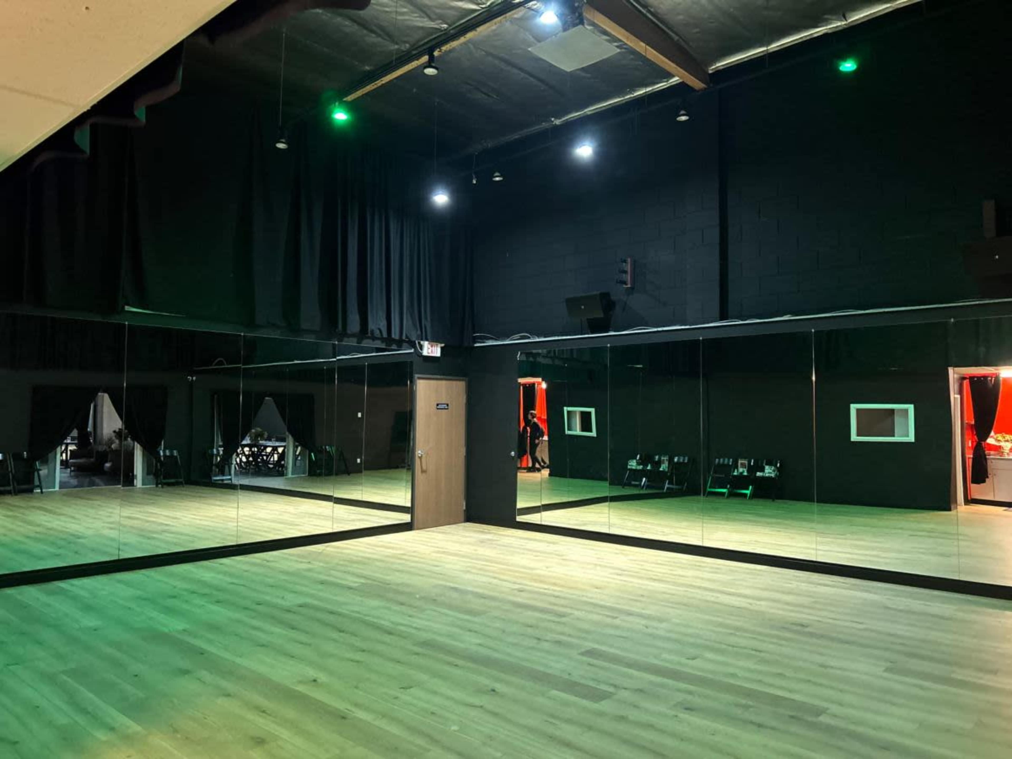 The image shows a large dance studio with mirrored walls, wooden flooring, and dim lighting.