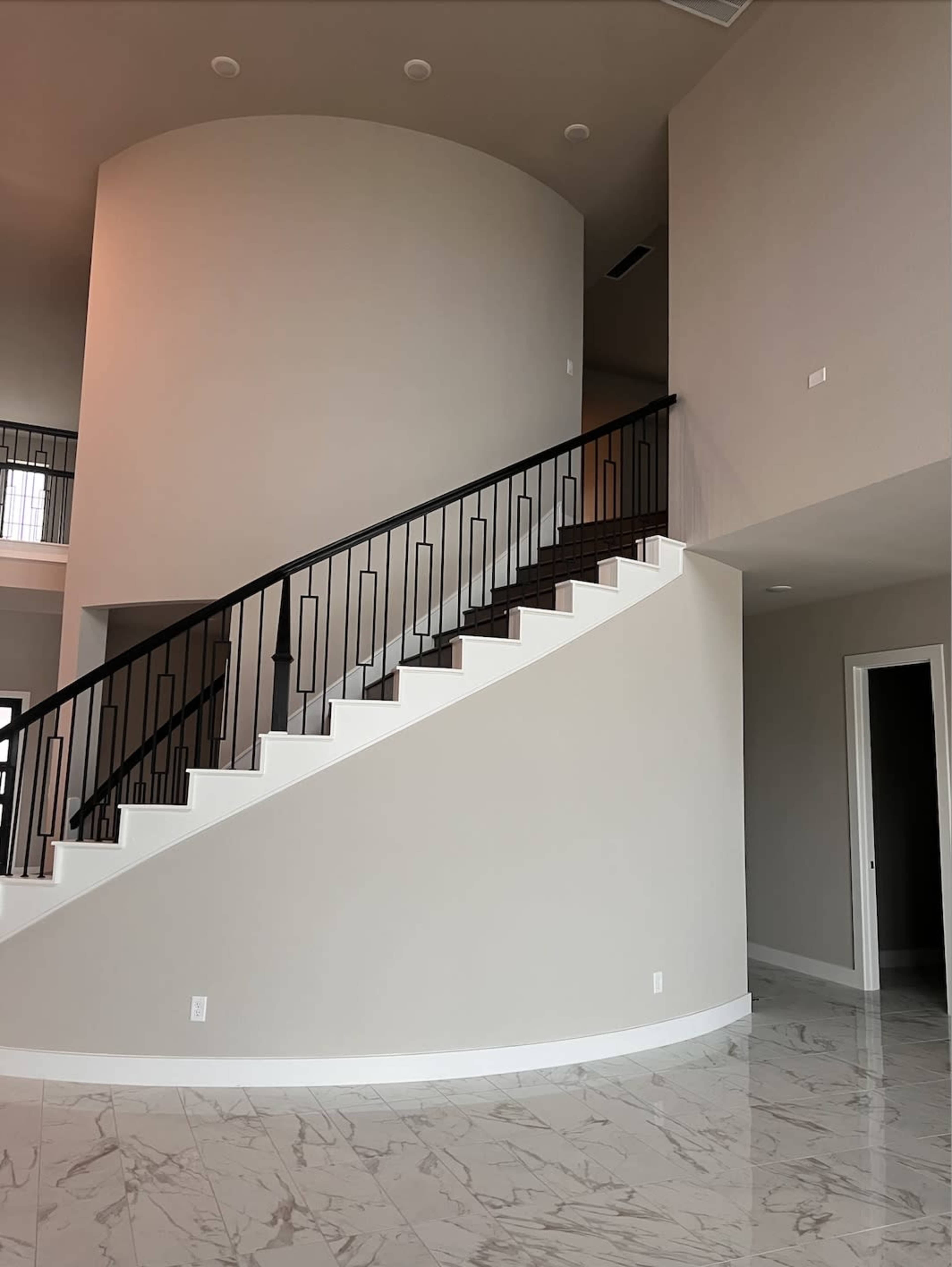 The image shows an interior space featuring a curved staircase with white steps and a black railing, alongside a large circular wall and a glossy marble floor.