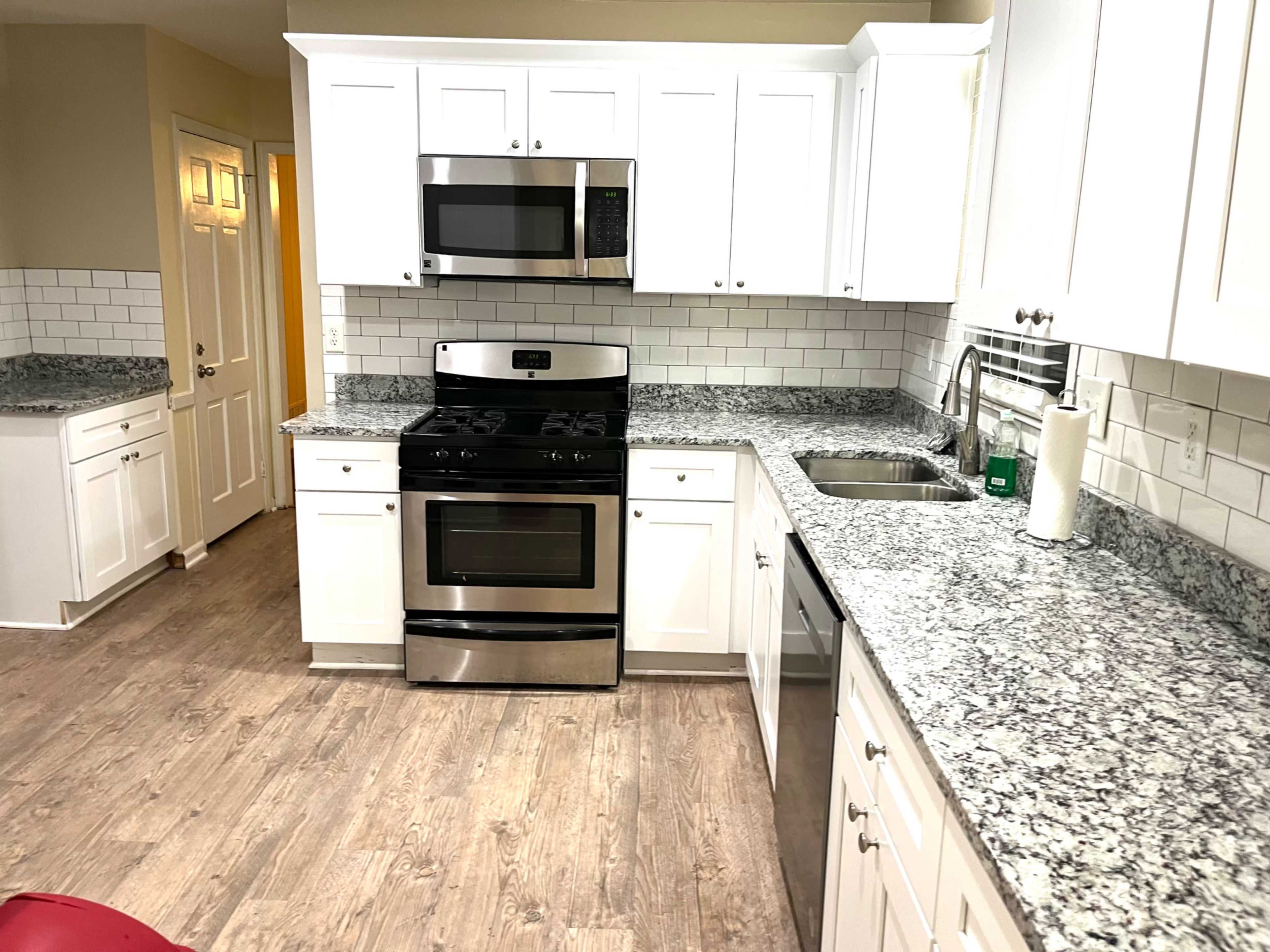 The image shows a modern kitchen with white cabinets, a stainless steel stove, and granite countertops.