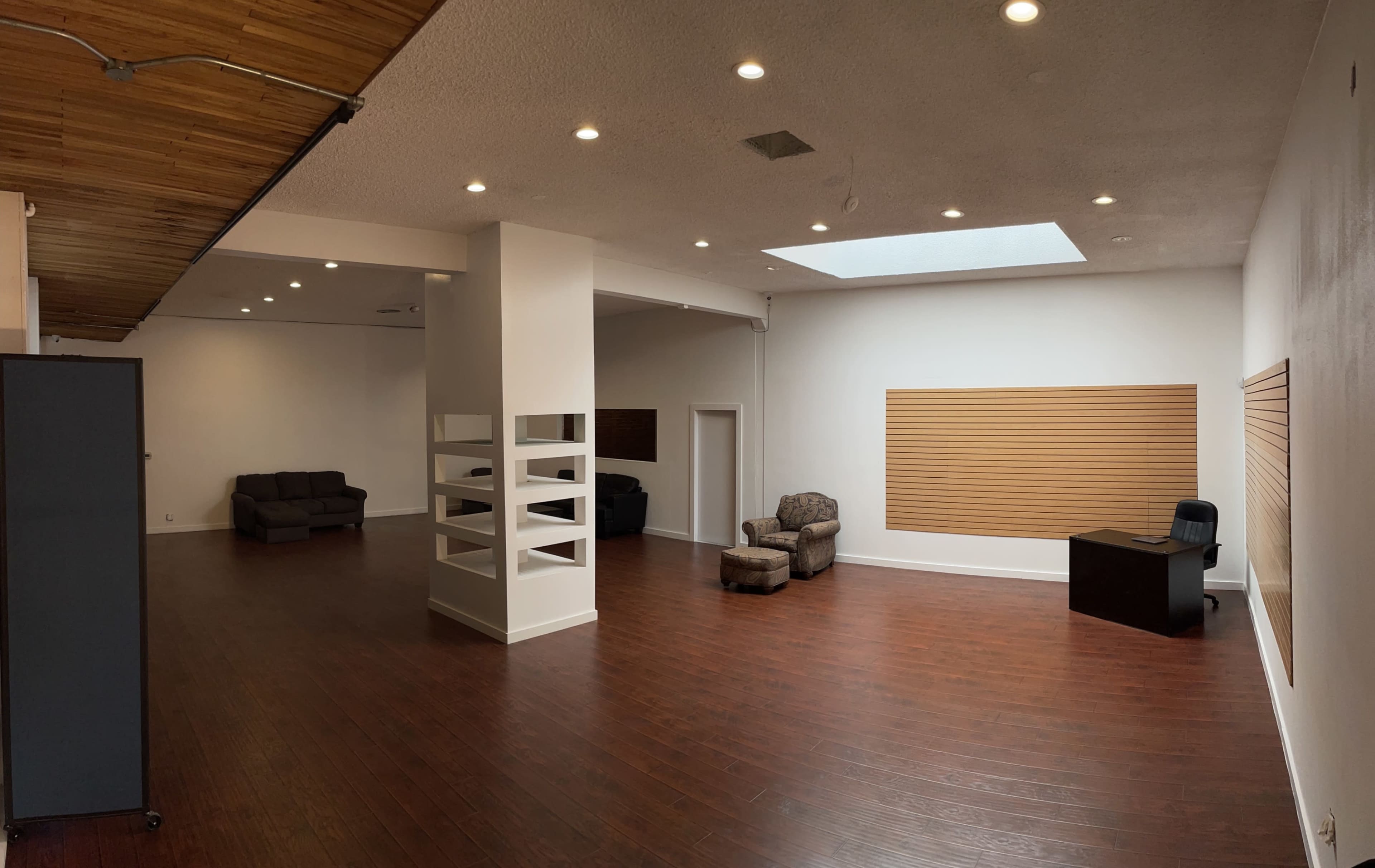 An empty and spacious room with hardwood floors, two seating areas, and a large skylight.