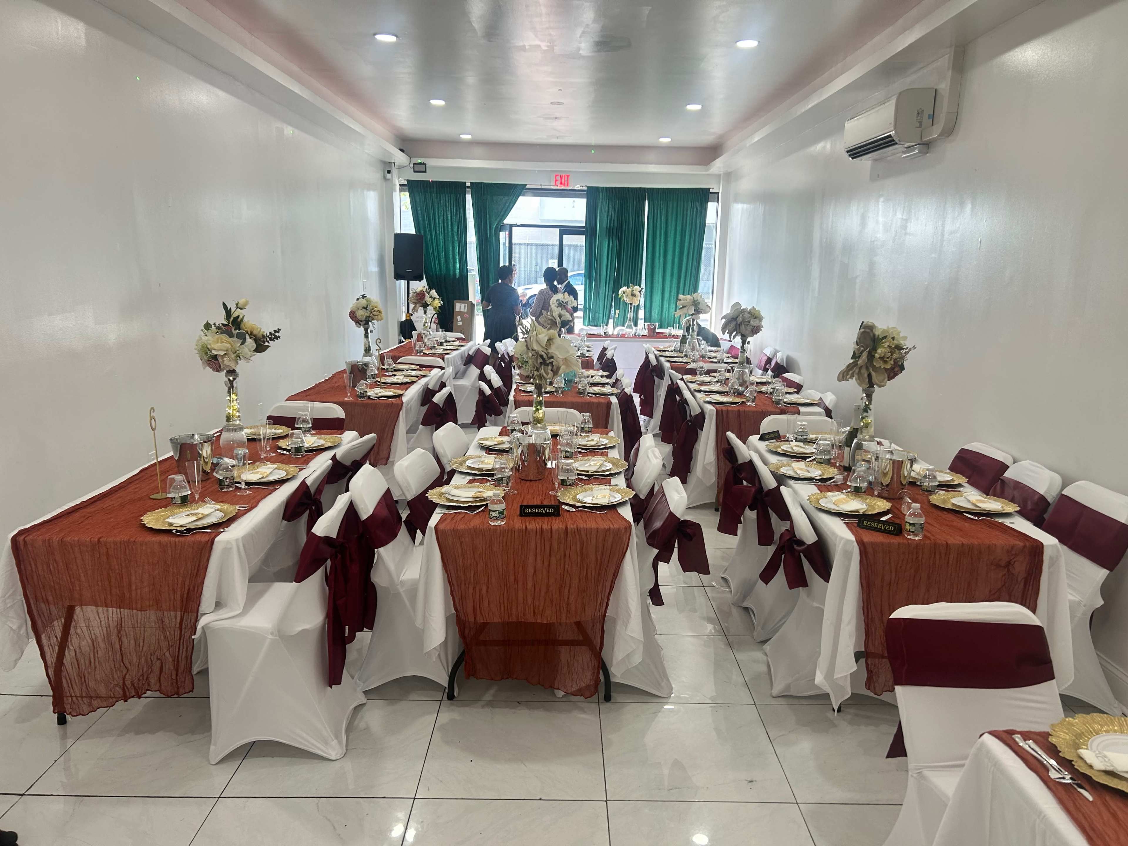 The image shows a banquet hall with several tables set for dining, featuring white and burgundy decorations, plates, and centerpieces.