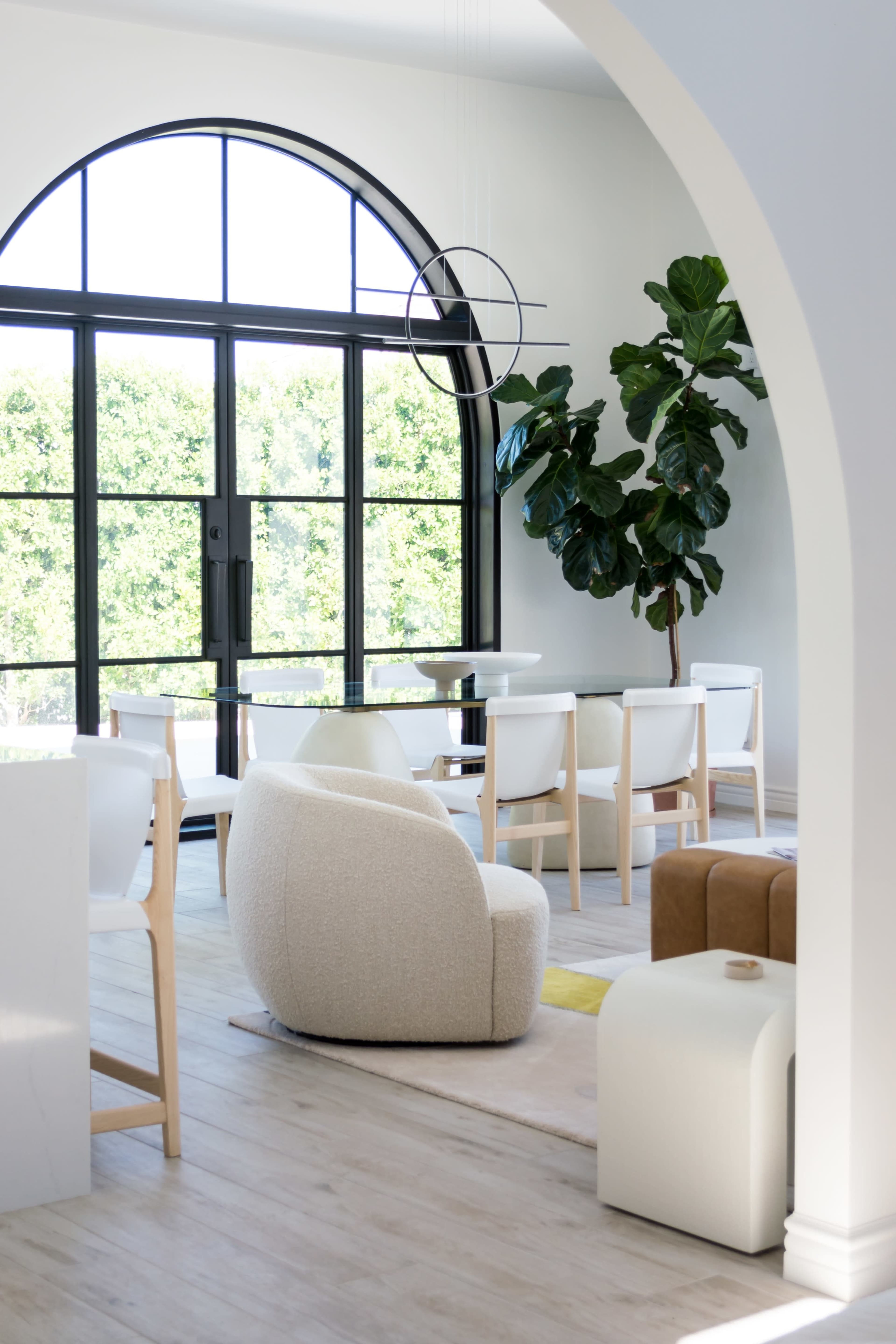 A modern, light-filled interior features a rounded chair, dining table, and large windows overlooking greenery.