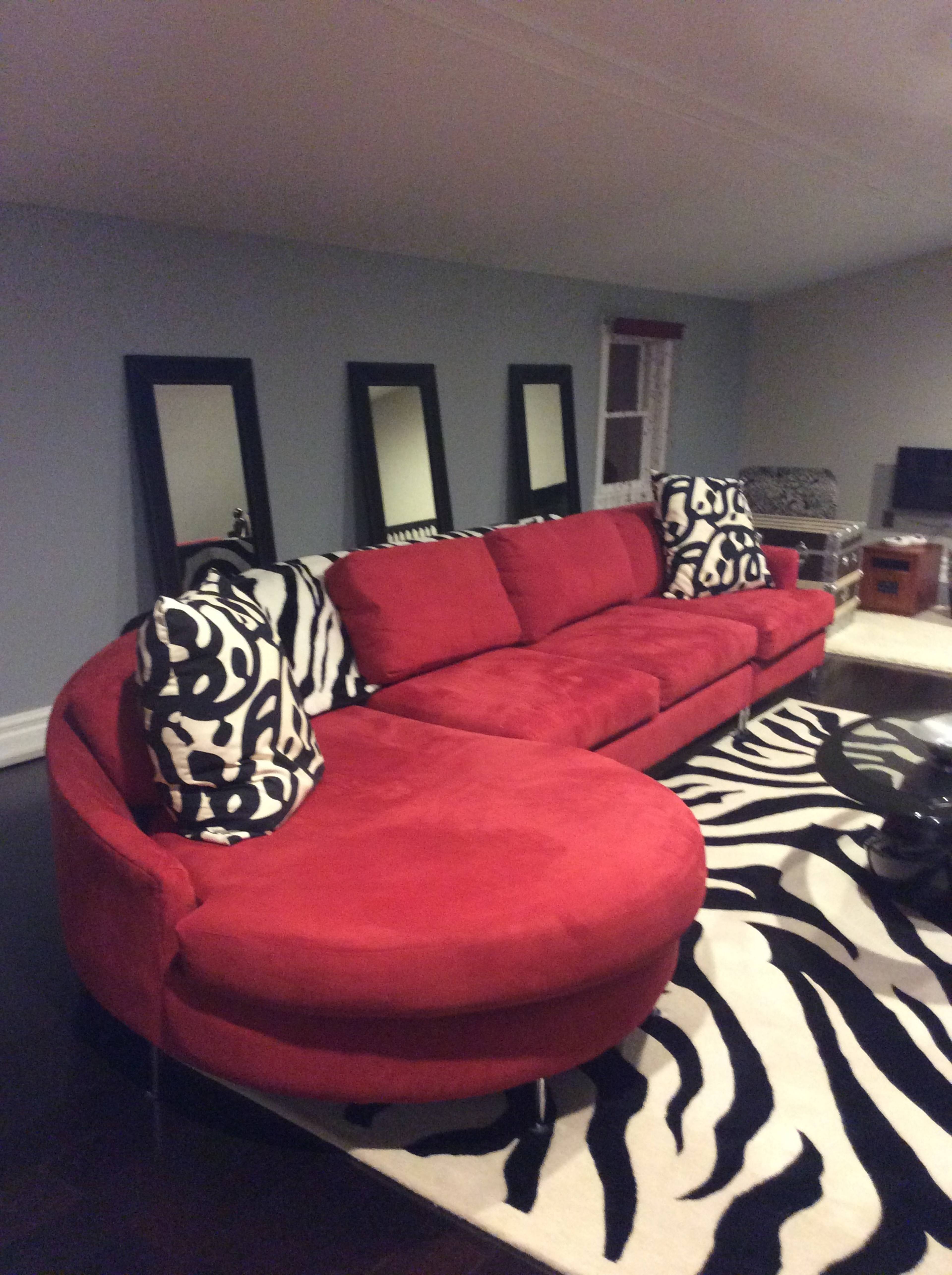 A red sectional sofa with black and white zebra print pillows, placed on a zebra print rug in a room with gray walls and mirrored accents.