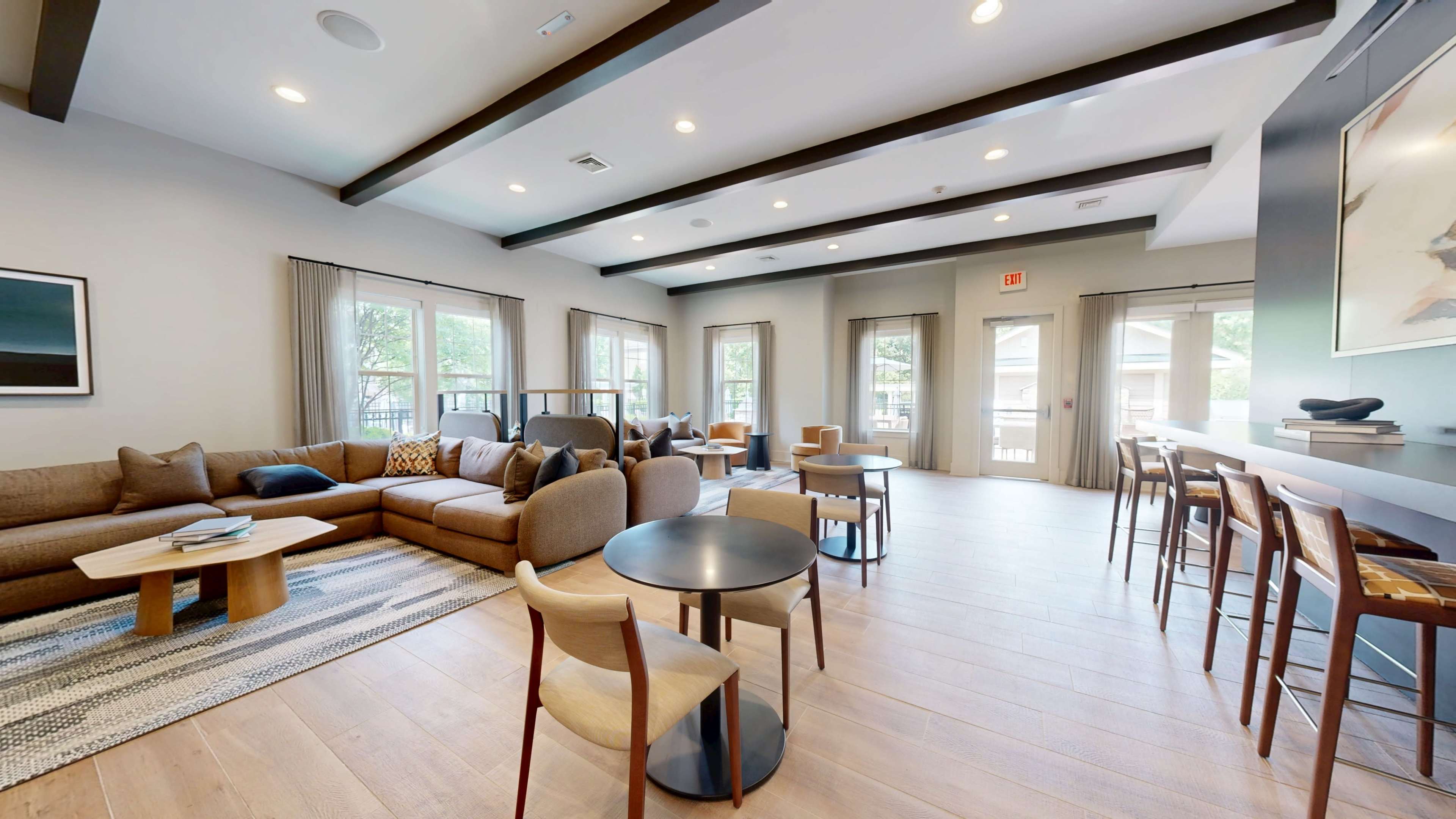 The image shows a modern living space with a sectional sofa, various seating arrangements, and large windows allowing natural light.