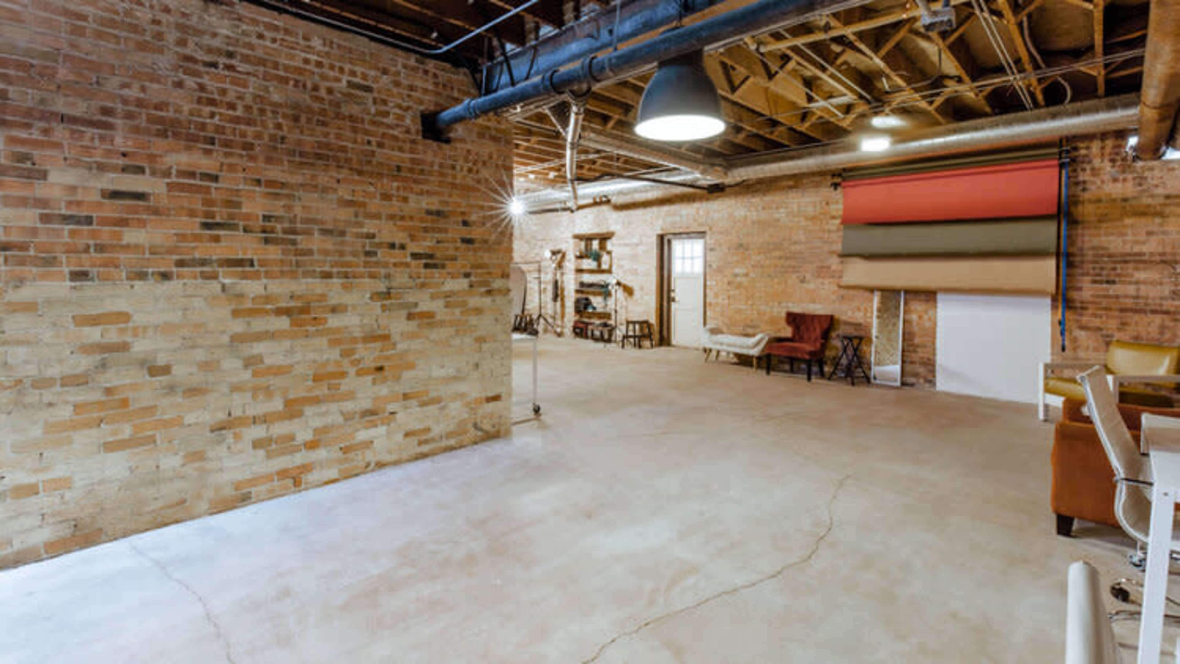 A spacious, unfinished brick interior with exposed beams and various pieces of furniture arranged along one side.