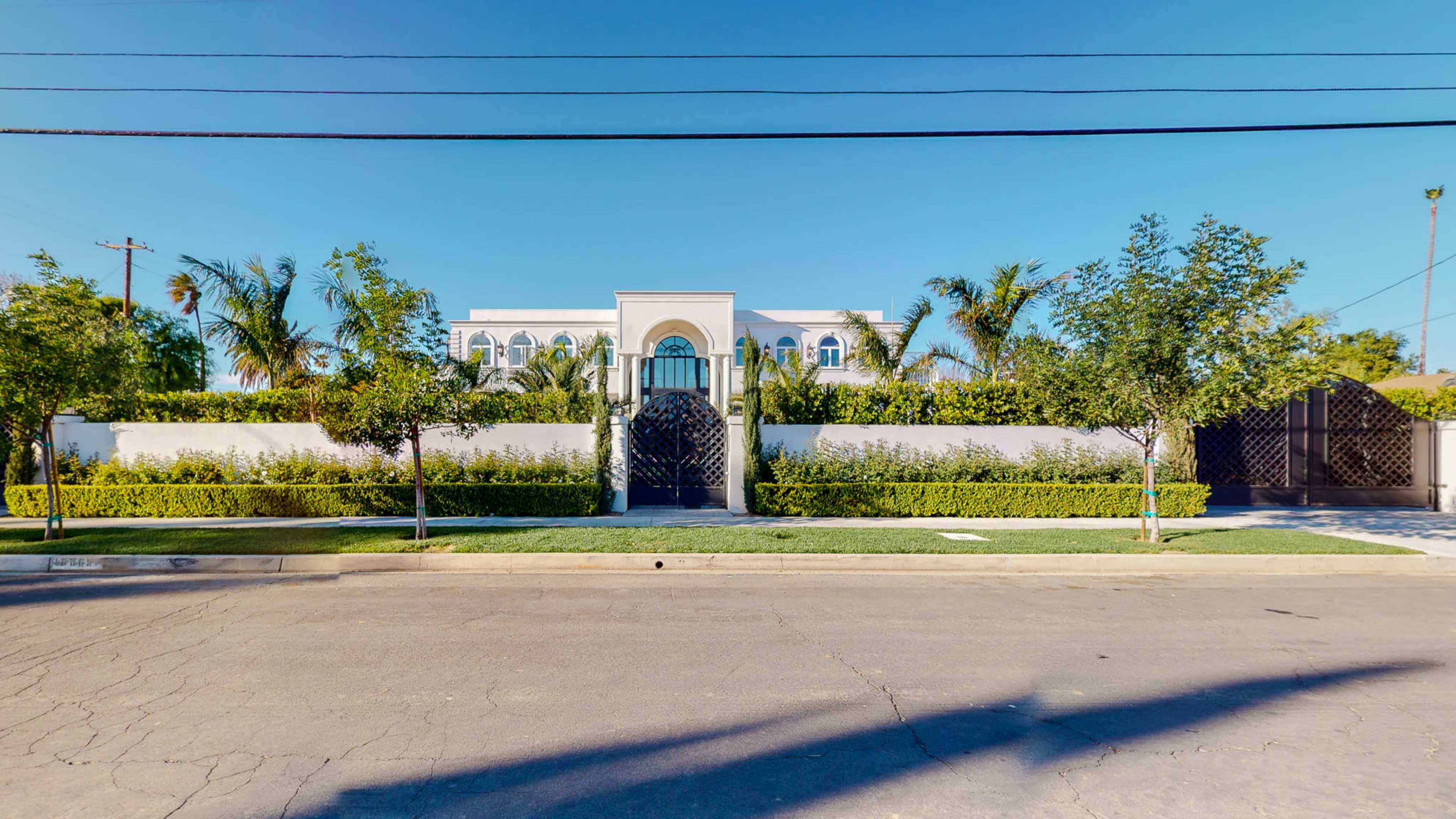 A large, modern house surrounded by greenery and a decorative gate, viewed from the street.
