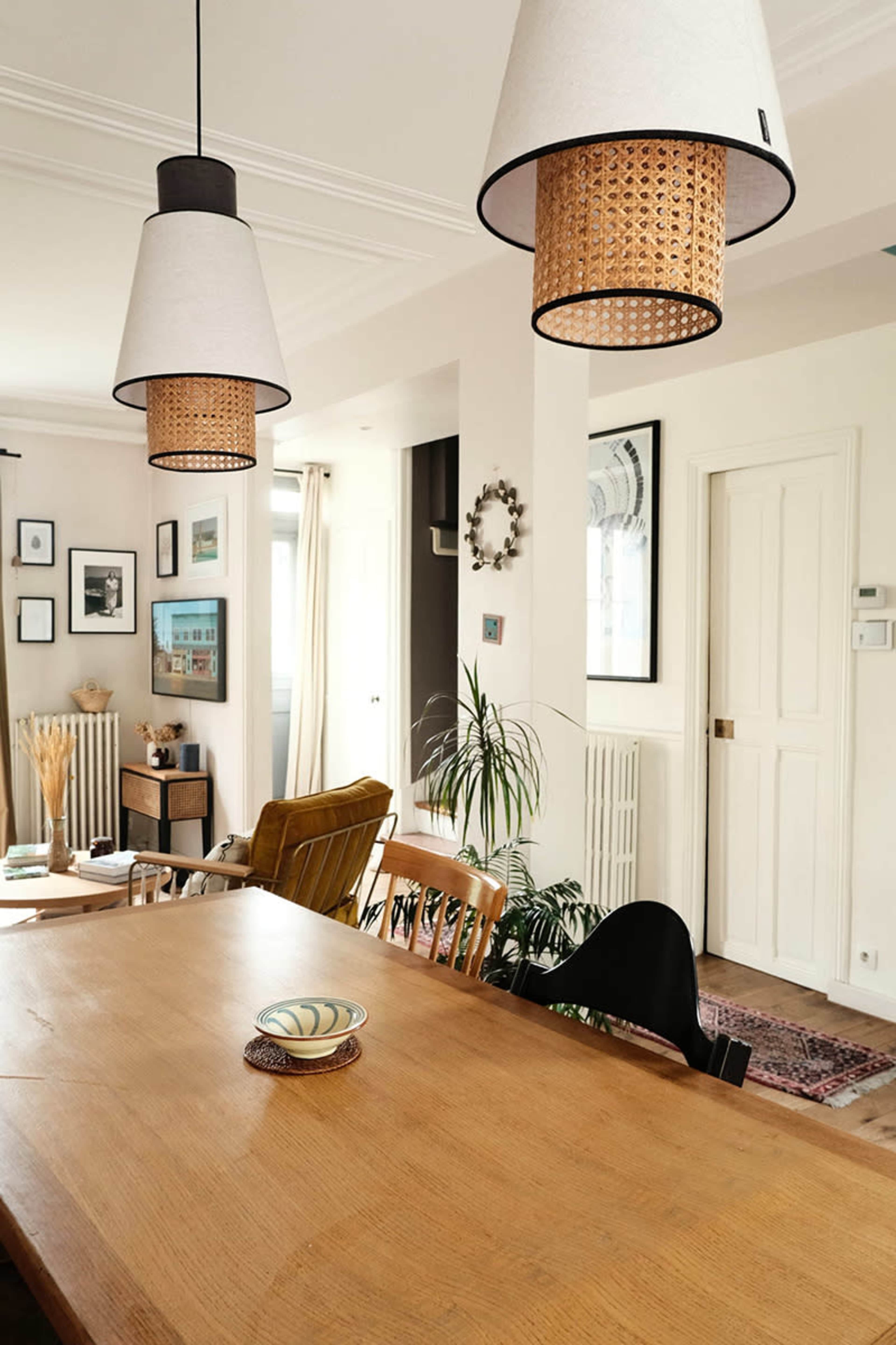 The image features a well-lit dining area with wooden furniture, including a table and chairs, and three pendant lights hanging overhead.
