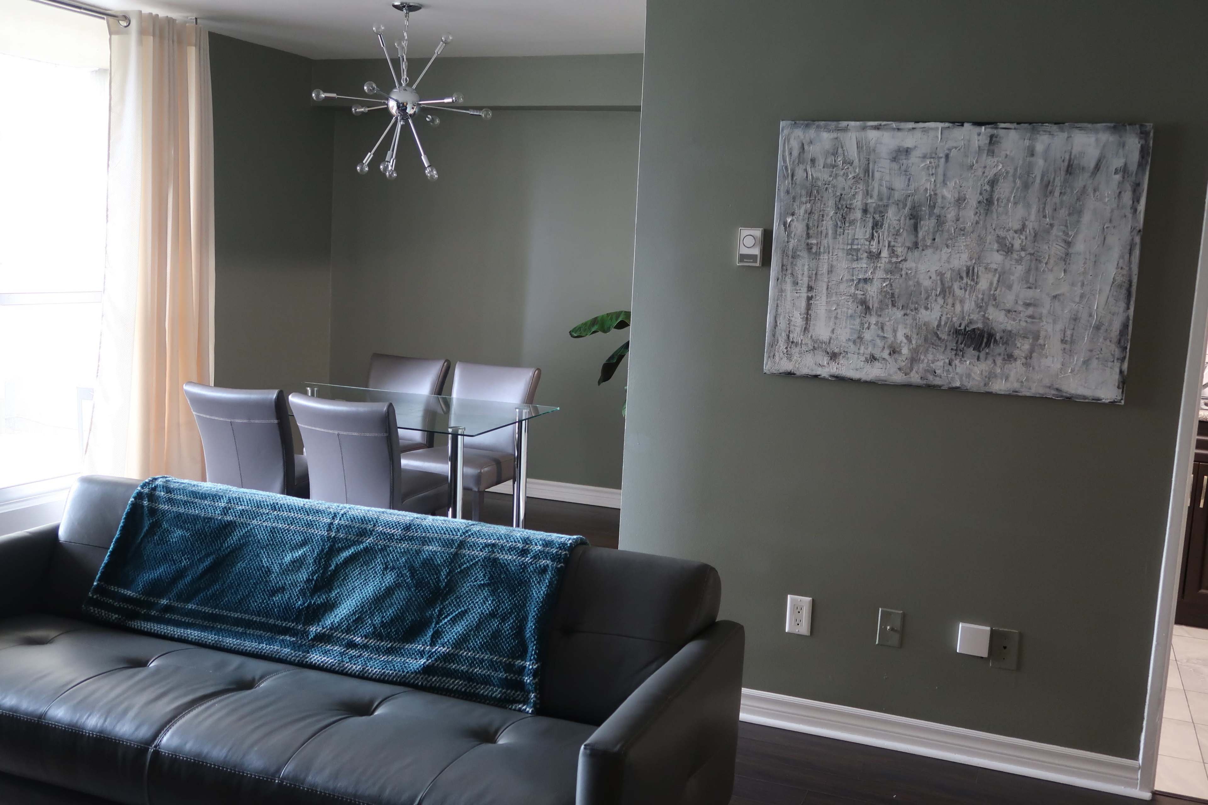 A modern living area featuring a gray couch with a blue throw blanket, adjacent to a glass dining table with four chairs in a softly lit interior.