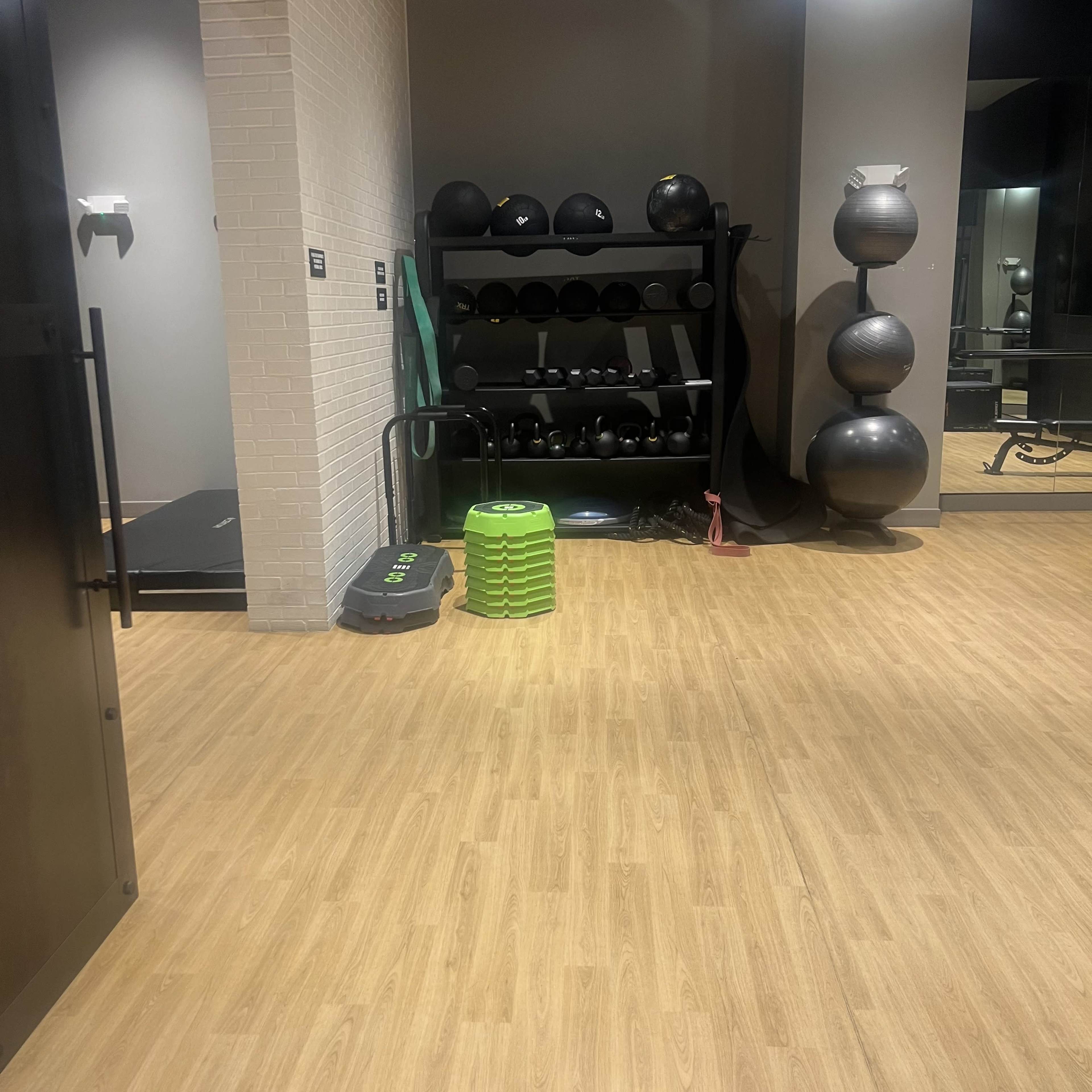 The image shows a fitness area featuring a rack of weights, a green exercise step, and various fitness equipment on the floor.