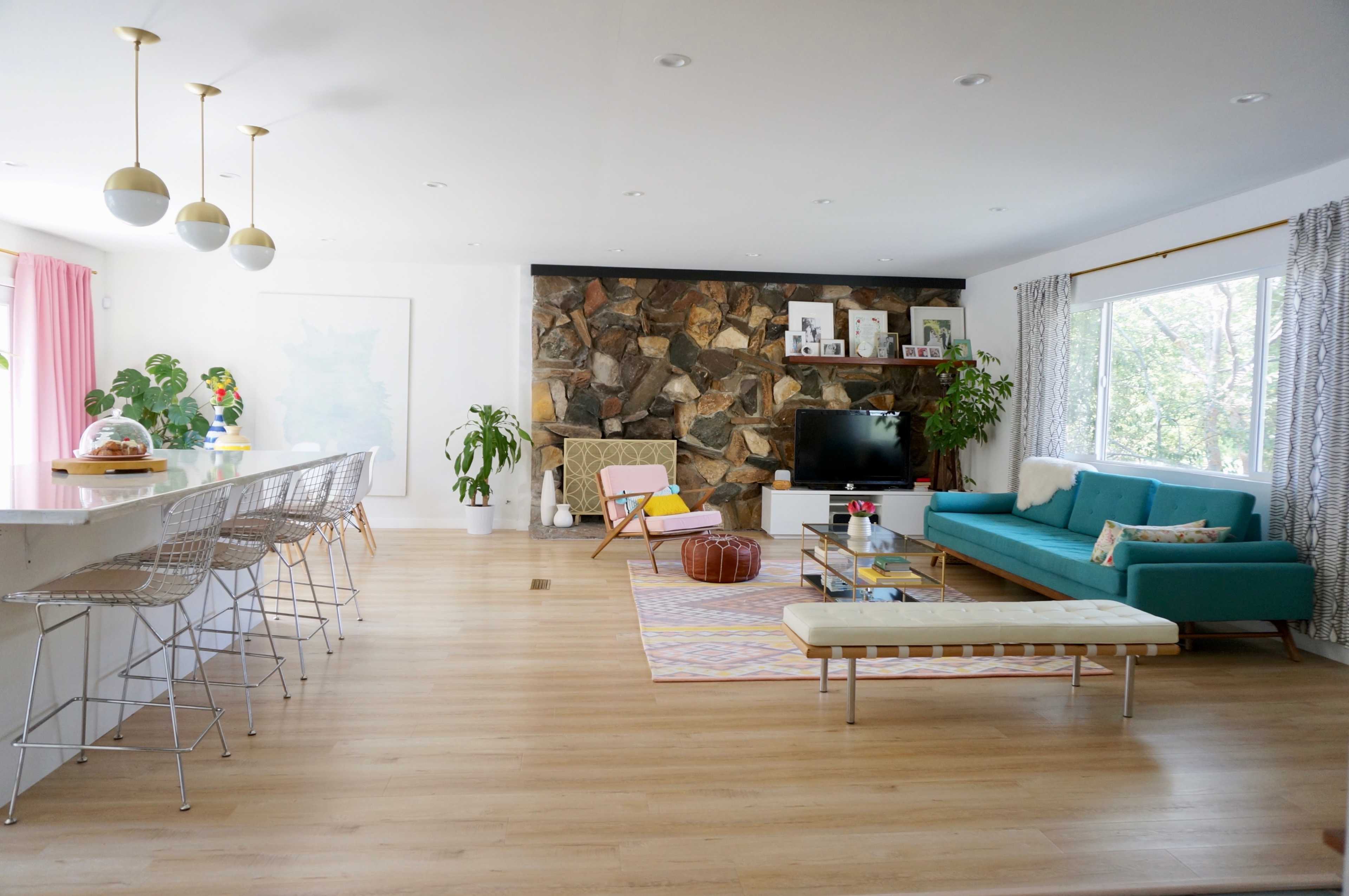 A modern living room with a stone wall, a teal sofa, a flat-screen TV, and a kitchen bar with stools.