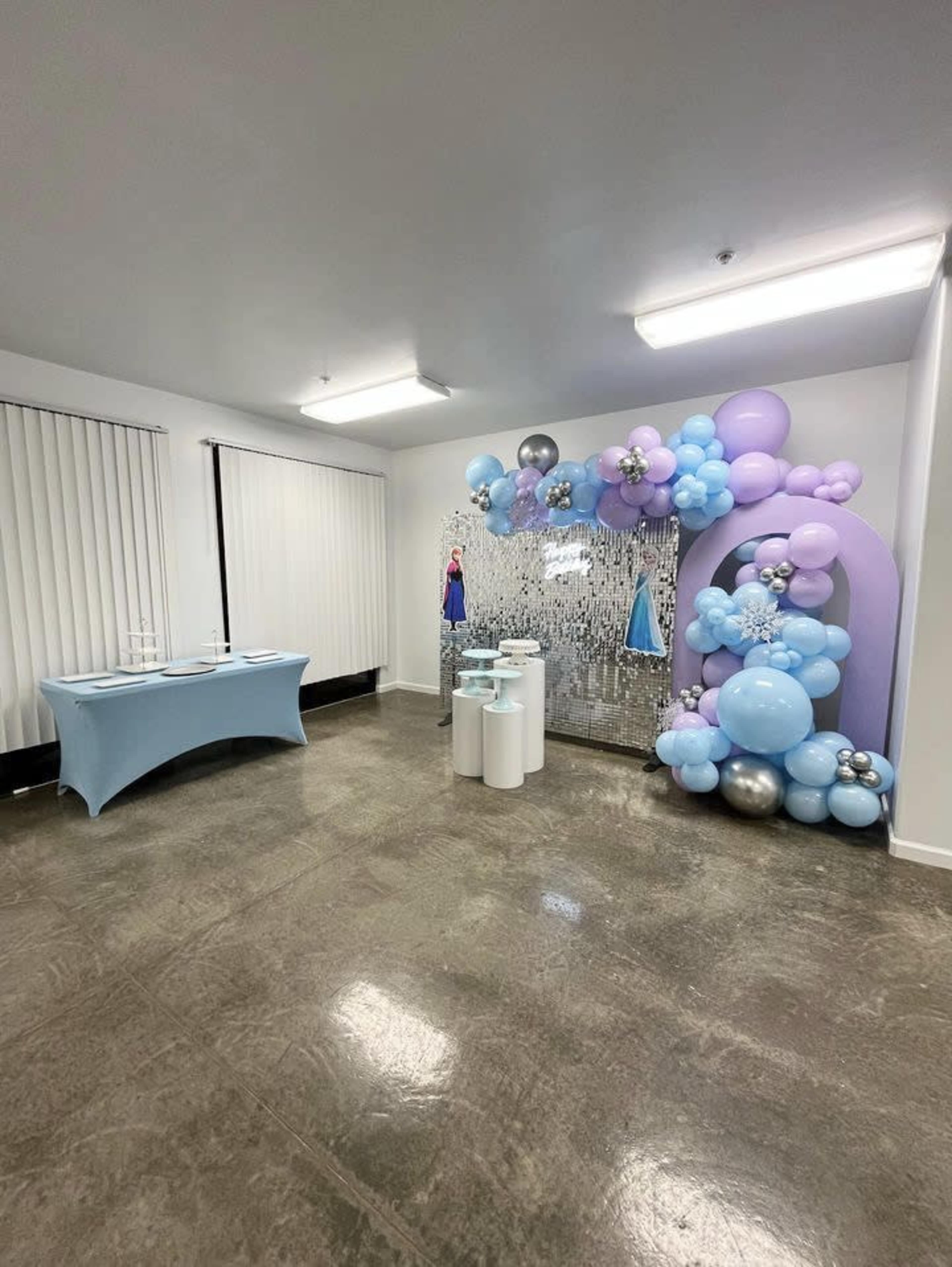 A decorated event space featuring a table on the left and a colorful balloon display with silver and blue accents on the right.