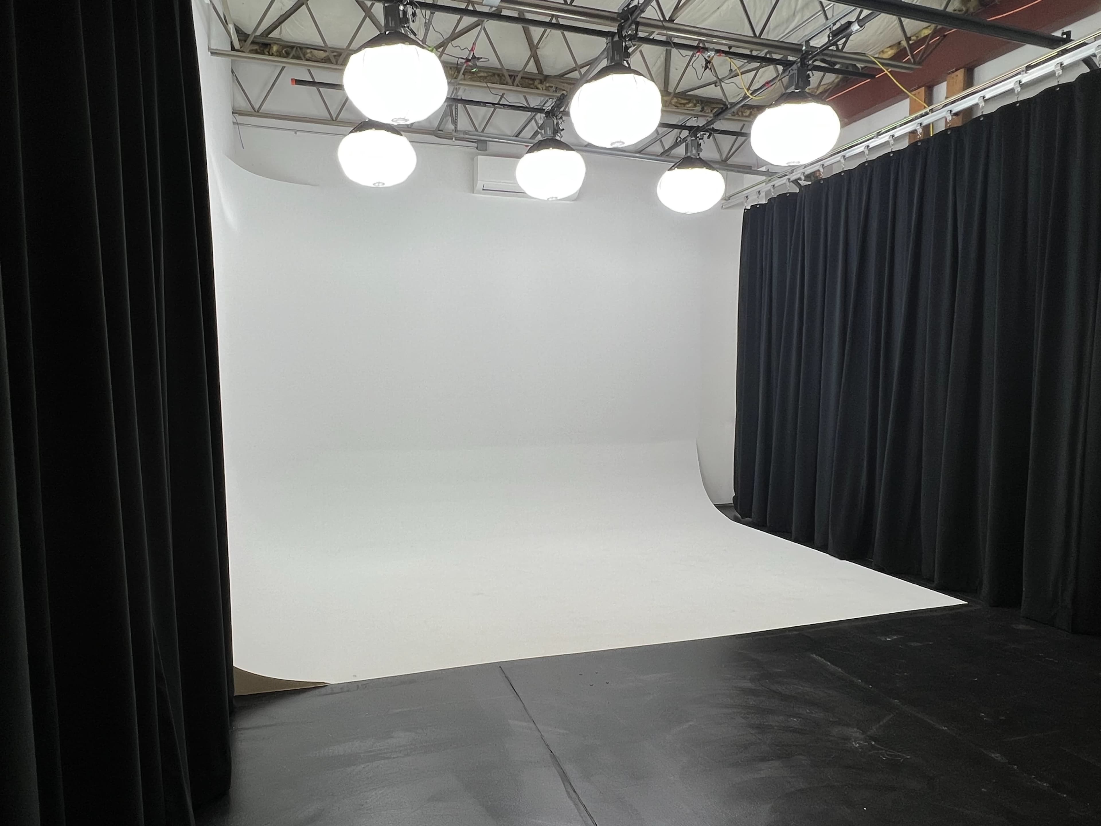 A photography studio with a seamless white backdrop, black curtains, and overhead lighting.