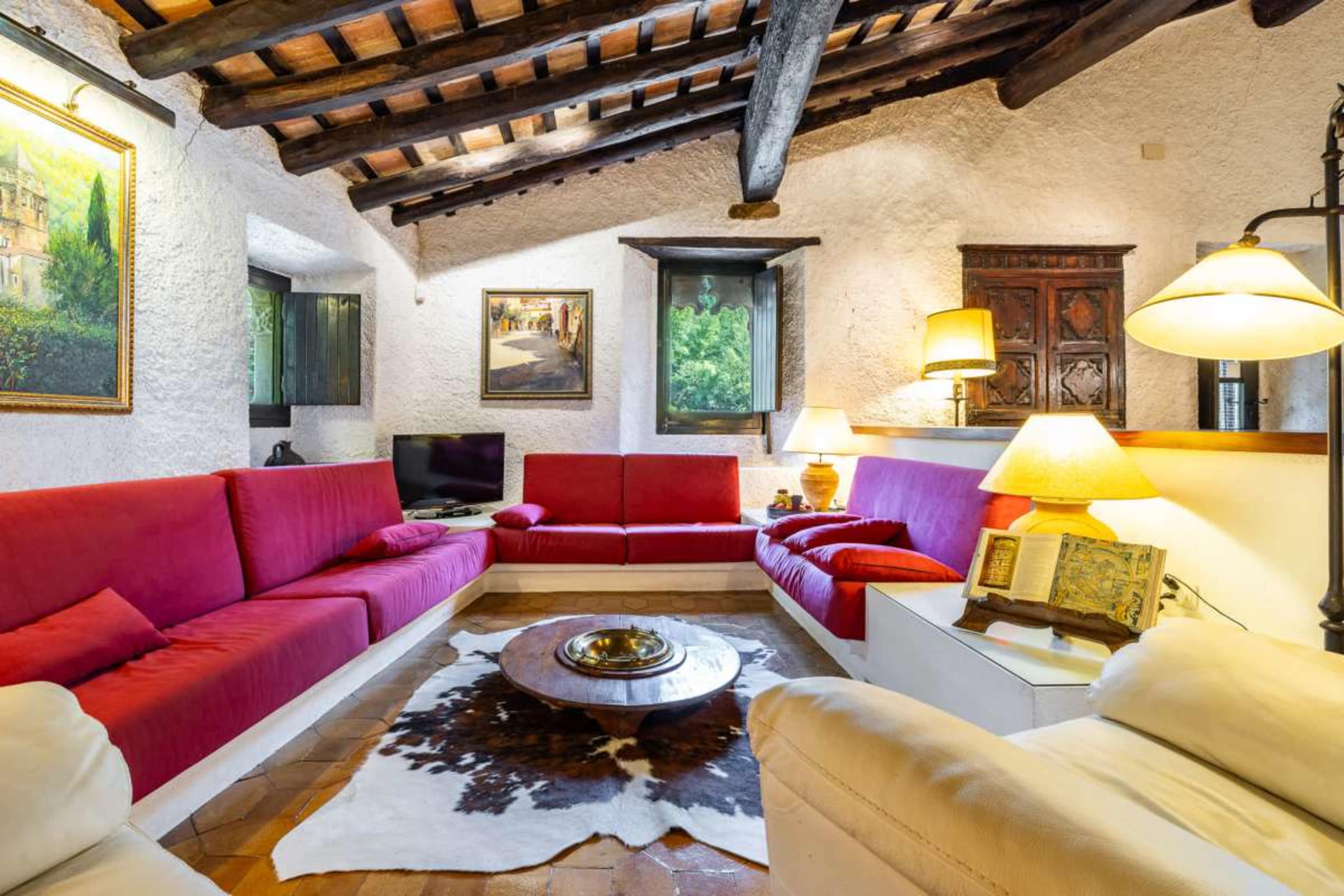 The image shows a cozy living room with red and white furniture, wooden beams, and a circular coffee table in the center.