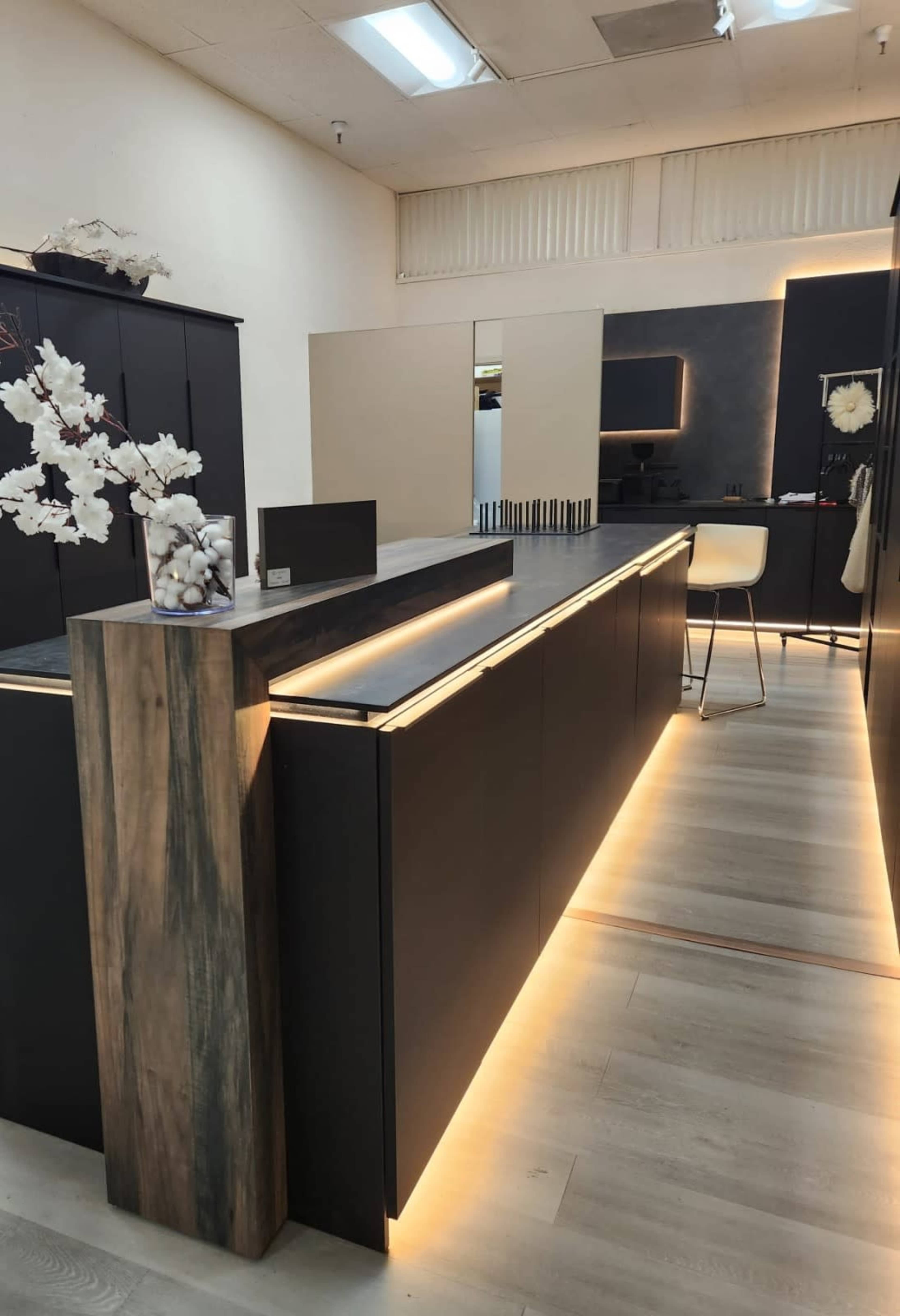 The image shows a modern kitchen design featuring dark cabinetry with under-cabinet lighting and a sleek countertop, complemented by a minimalist decor.