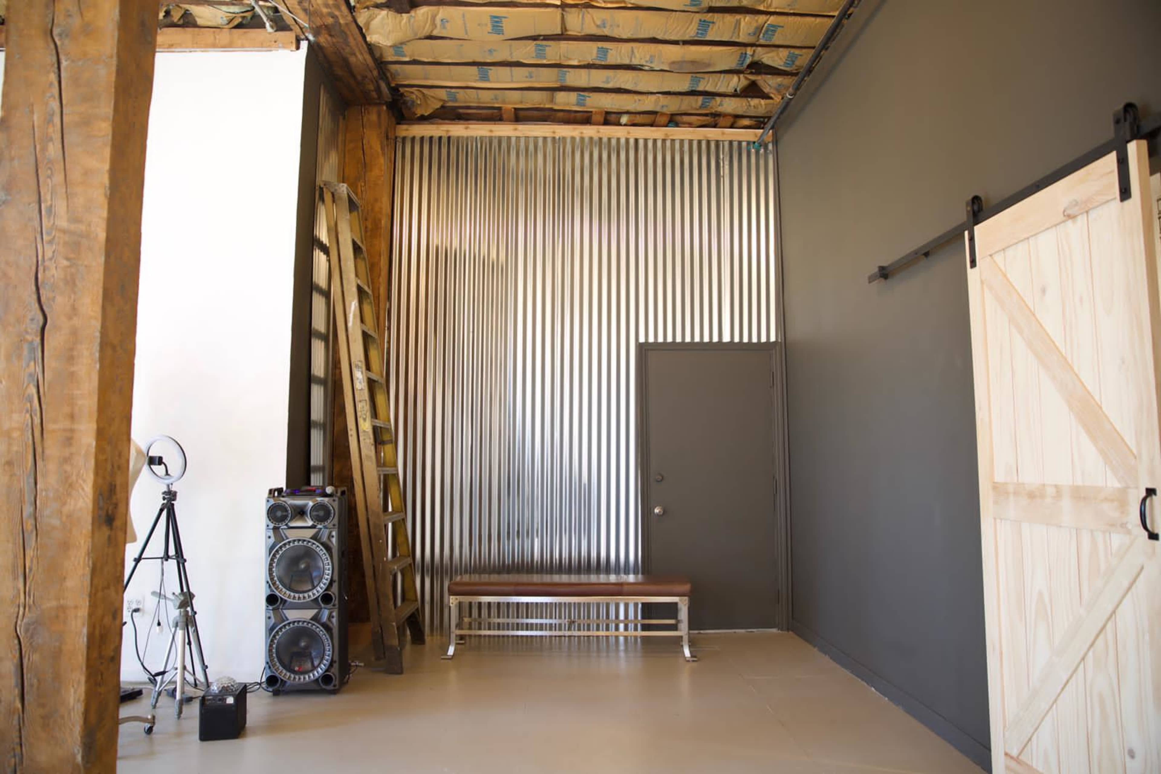 An industrial-style room with a corrugated metal wall, a wooden bench, a sliding barn door, and a ladder against the wall.