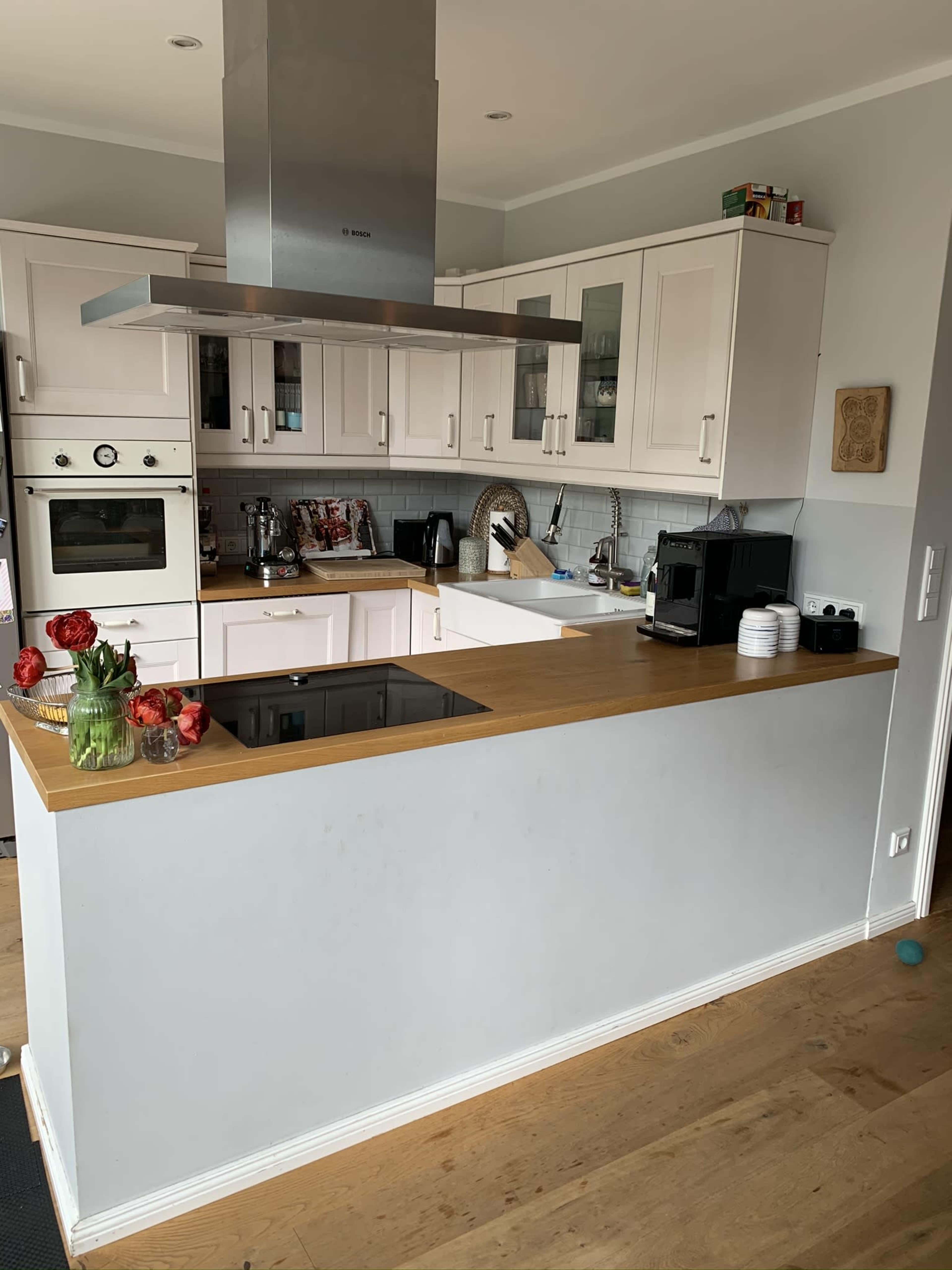 The image shows a modern kitchen with white cabinetry, a wooden countertop, and various appliances arranged on the counter.