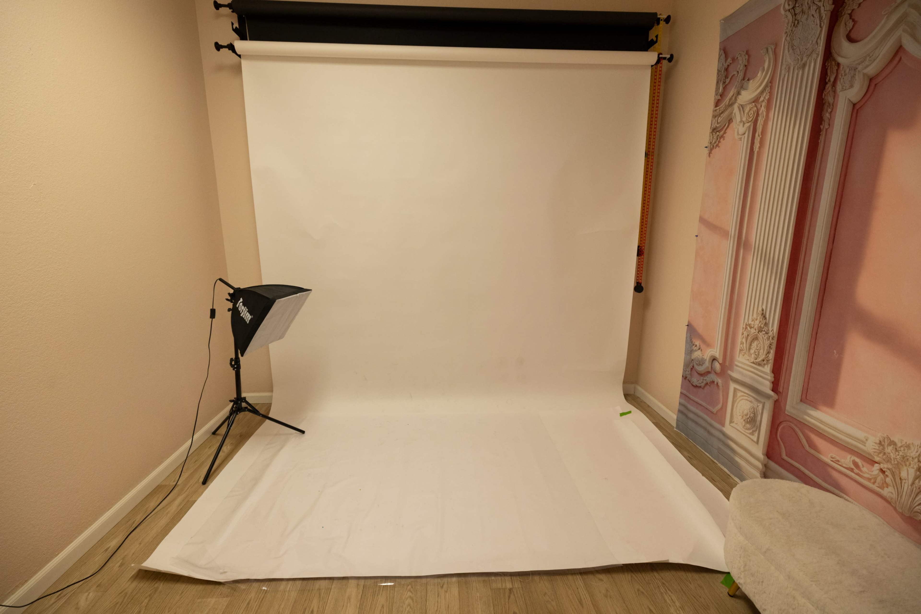 The image shows a photography studio setup with a white backdrop, a lighting fixture, and decorated walls.