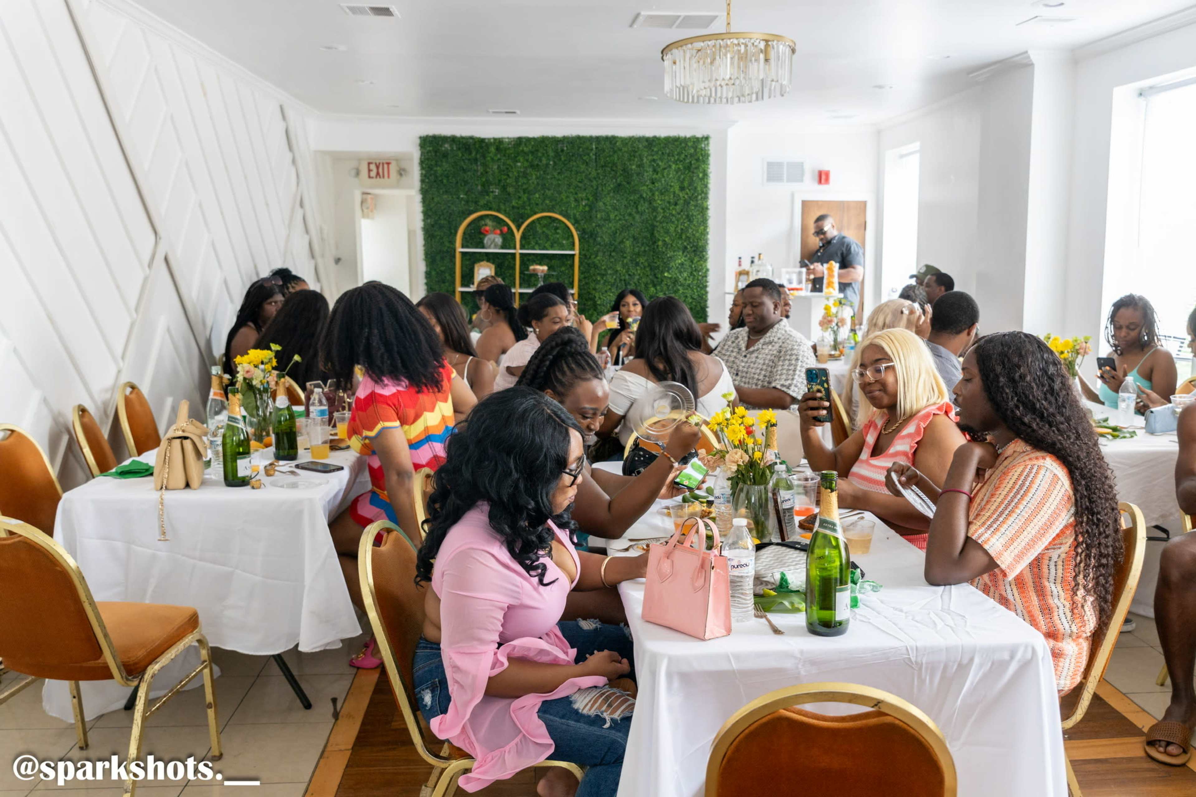 A group of people sits at tables adorned with flowers and drinks in a bright, modern dining space.