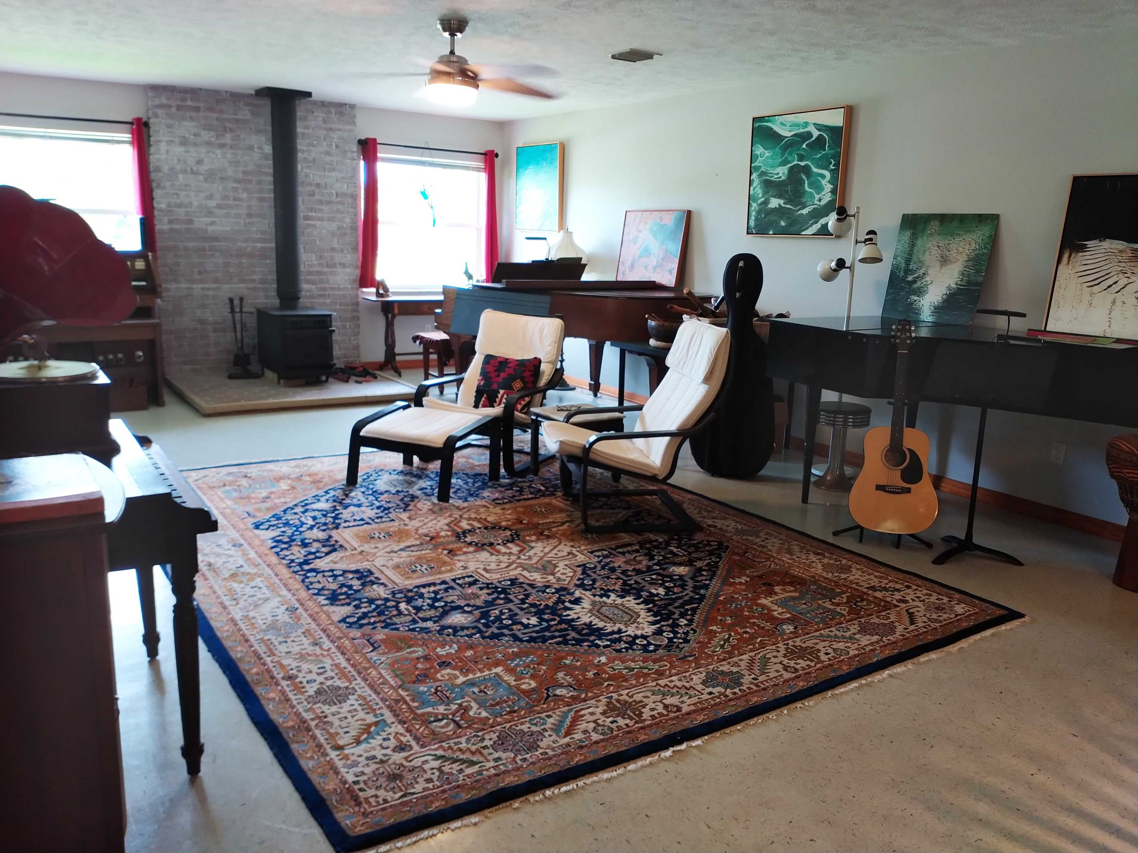 The room features a seating area with two chairs on a patterned rug, a piano, and various artworks displayed on the walls.