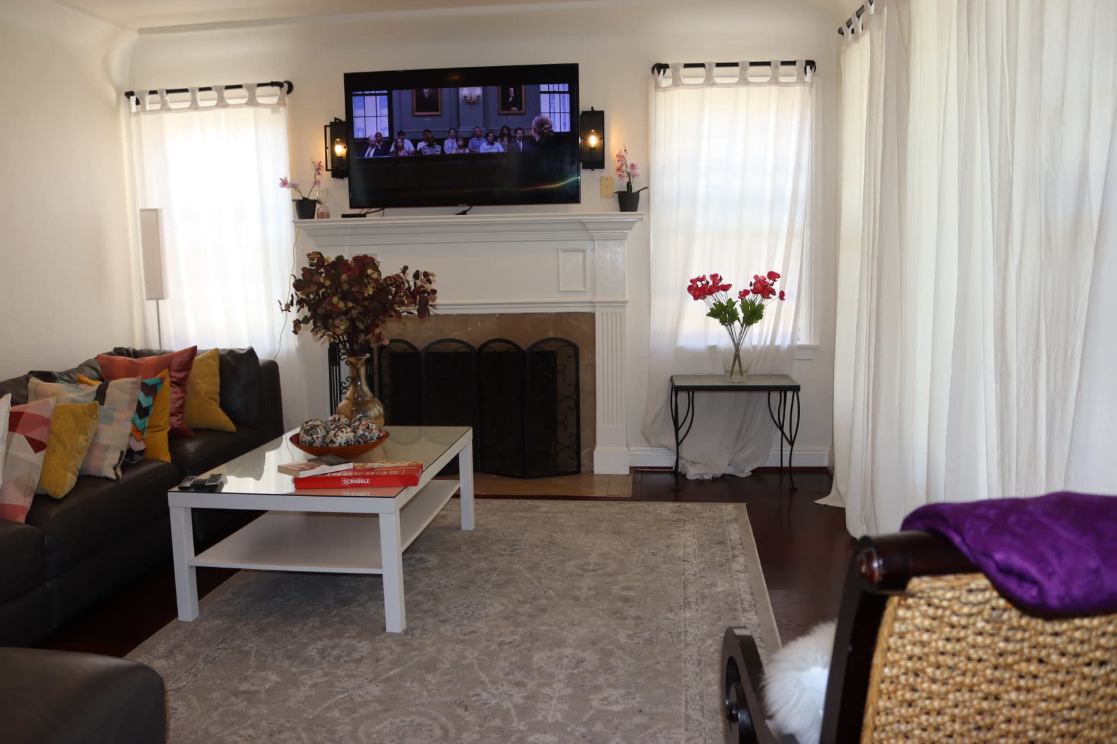A living room with a black leather sofa, a white coffee table, and a television mounted above a fireplace.