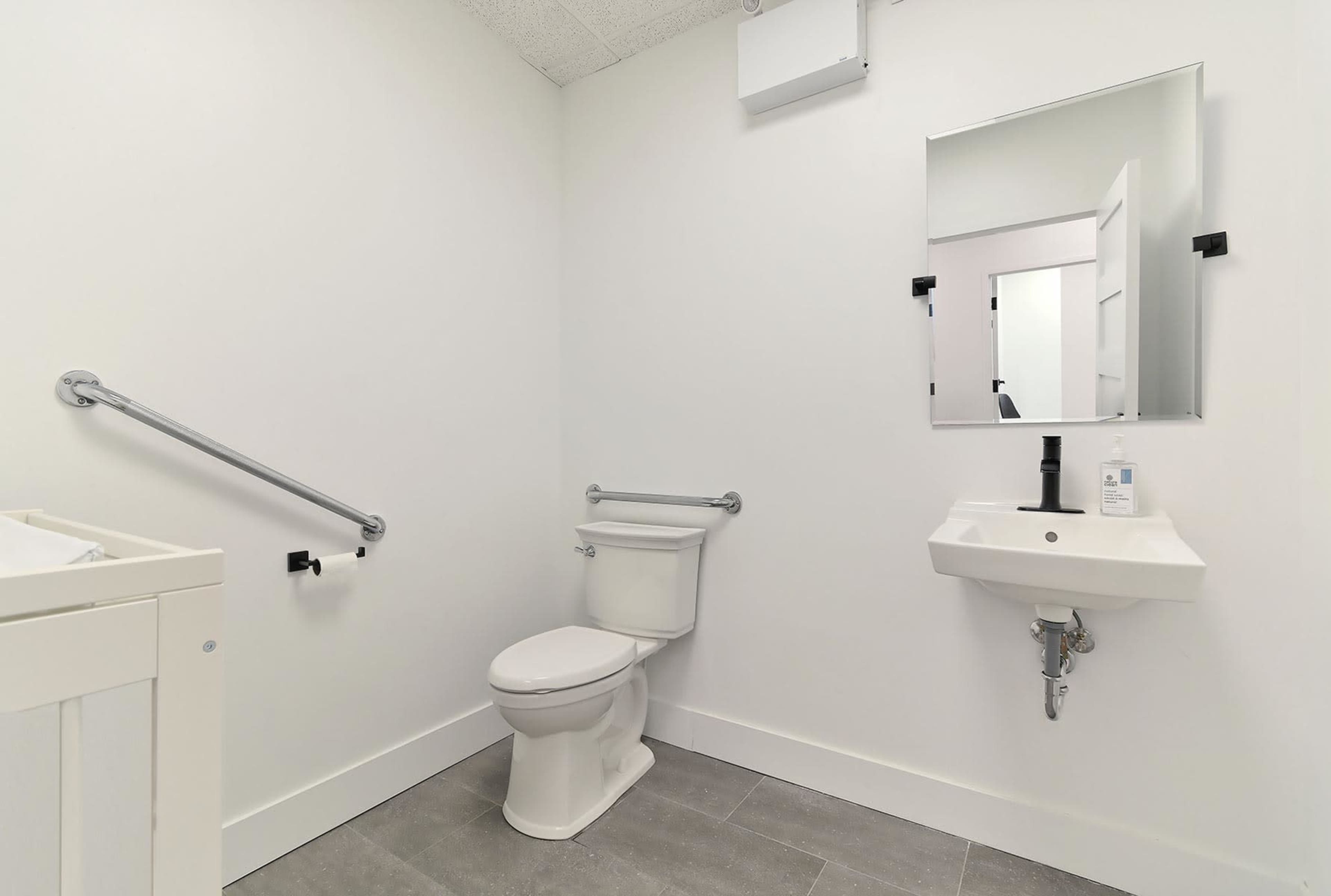 A clean, minimalist bathroom with a toilet, a small sink, and accessibility features such as grab bars on the walls.