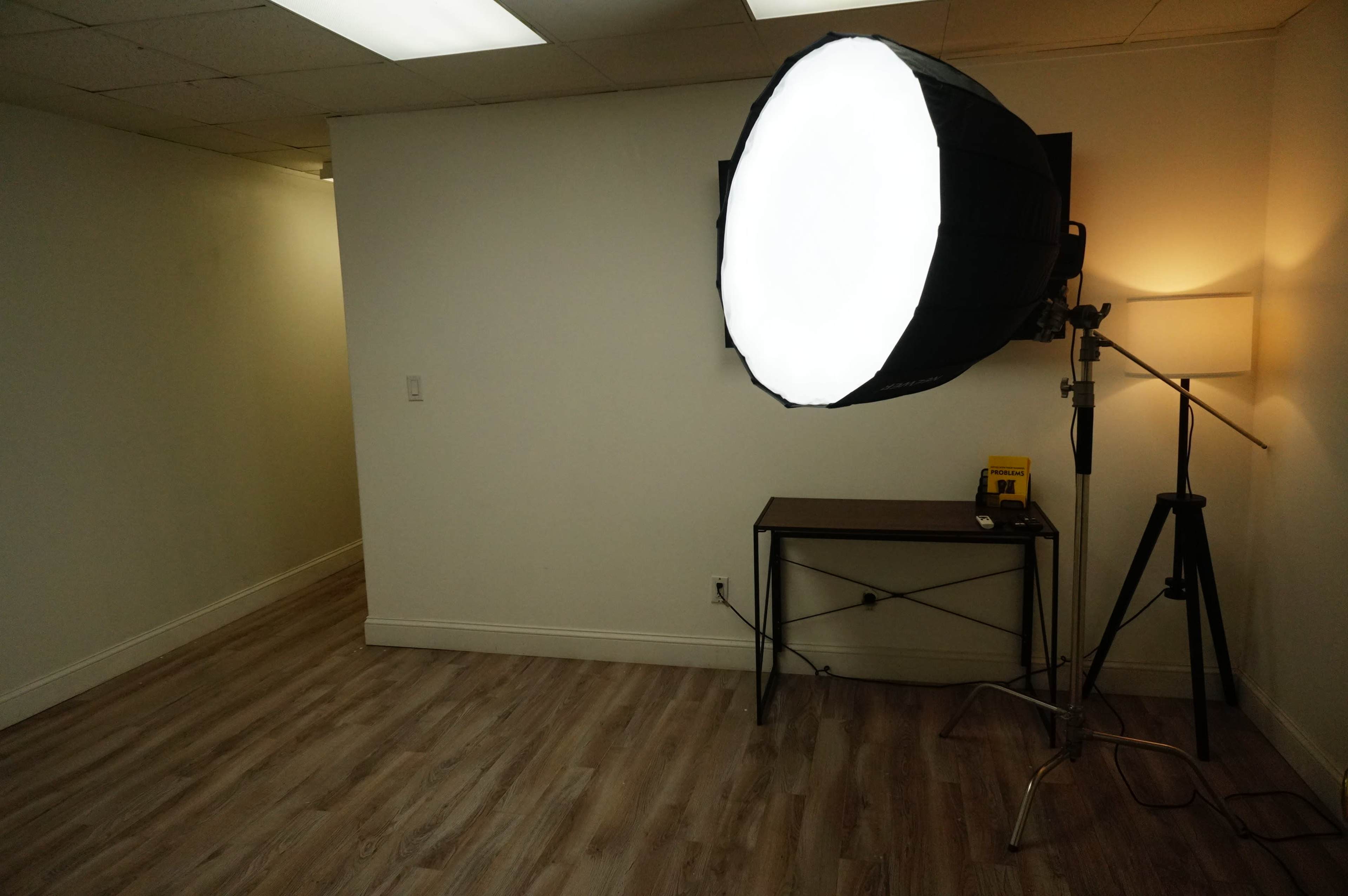 A well-lit room featuring a large softbox light on a stand and a small table against a plain wall.