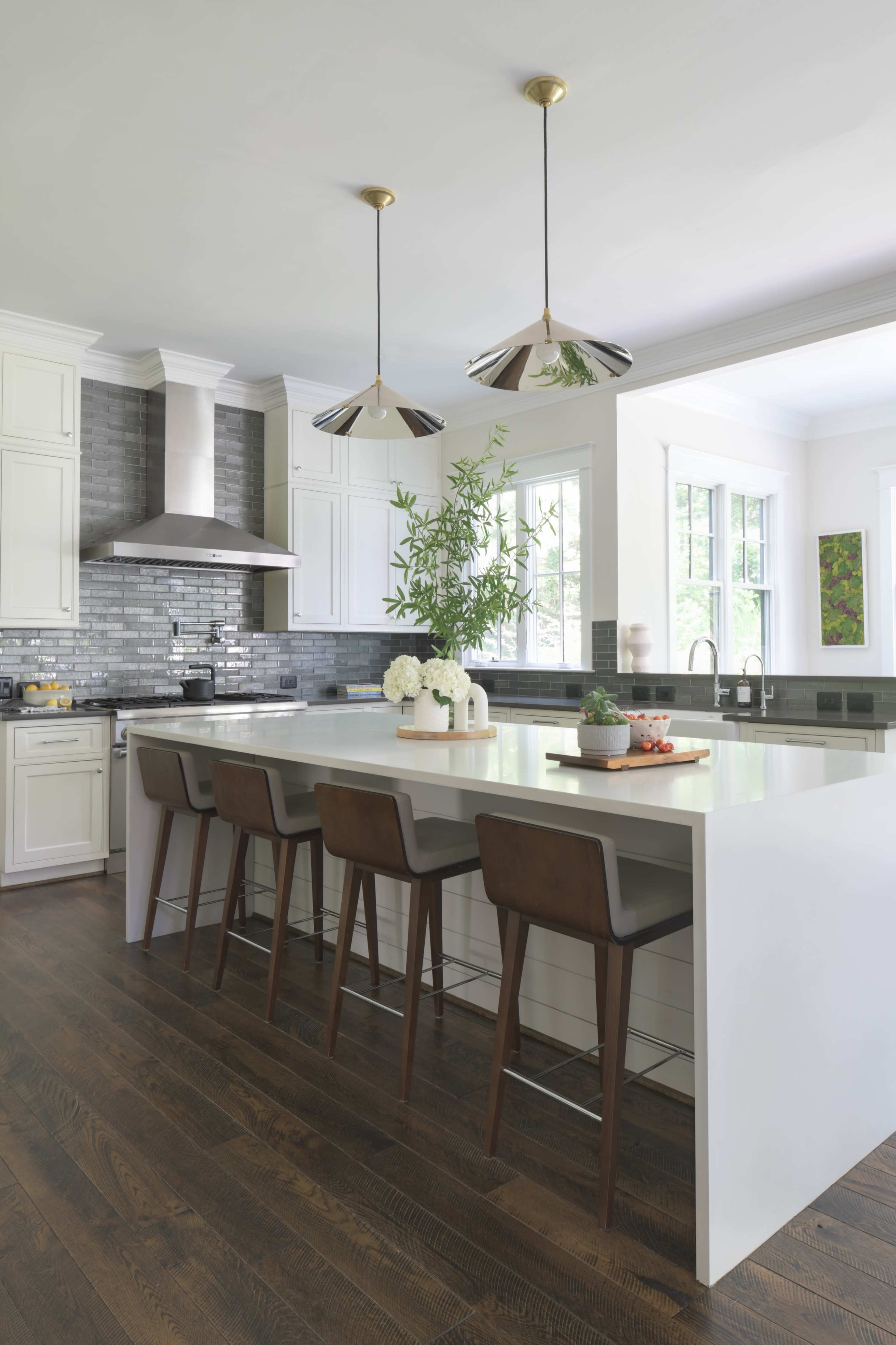 A modern kitchen features white cabinetry, a large island with seating, and pendant lighting.