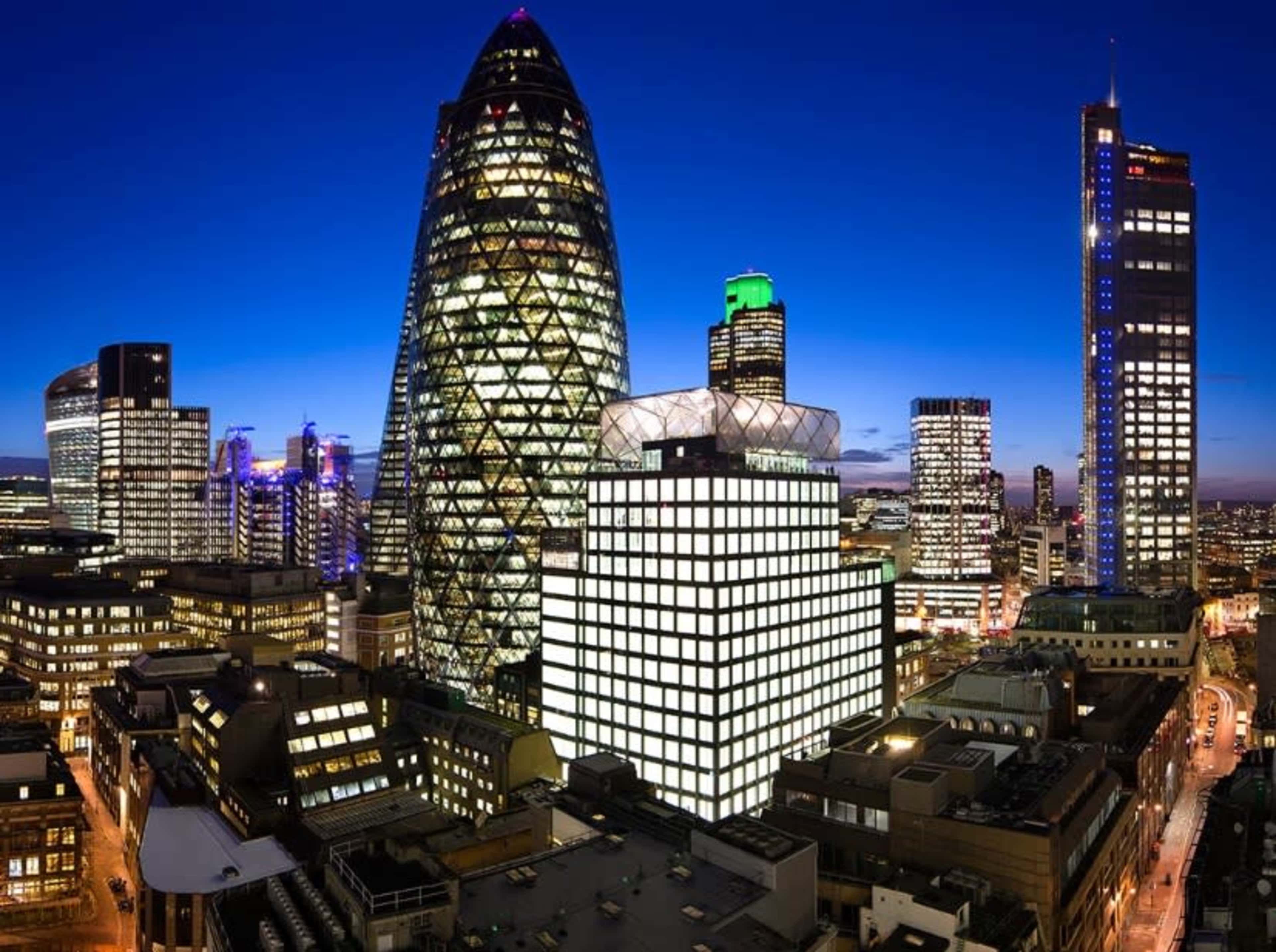 The scene shows a city skyline at dusk featuring modern skyscrapers, including the distinctive Gherkin building, with city lights beginning to illuminate the streets below.