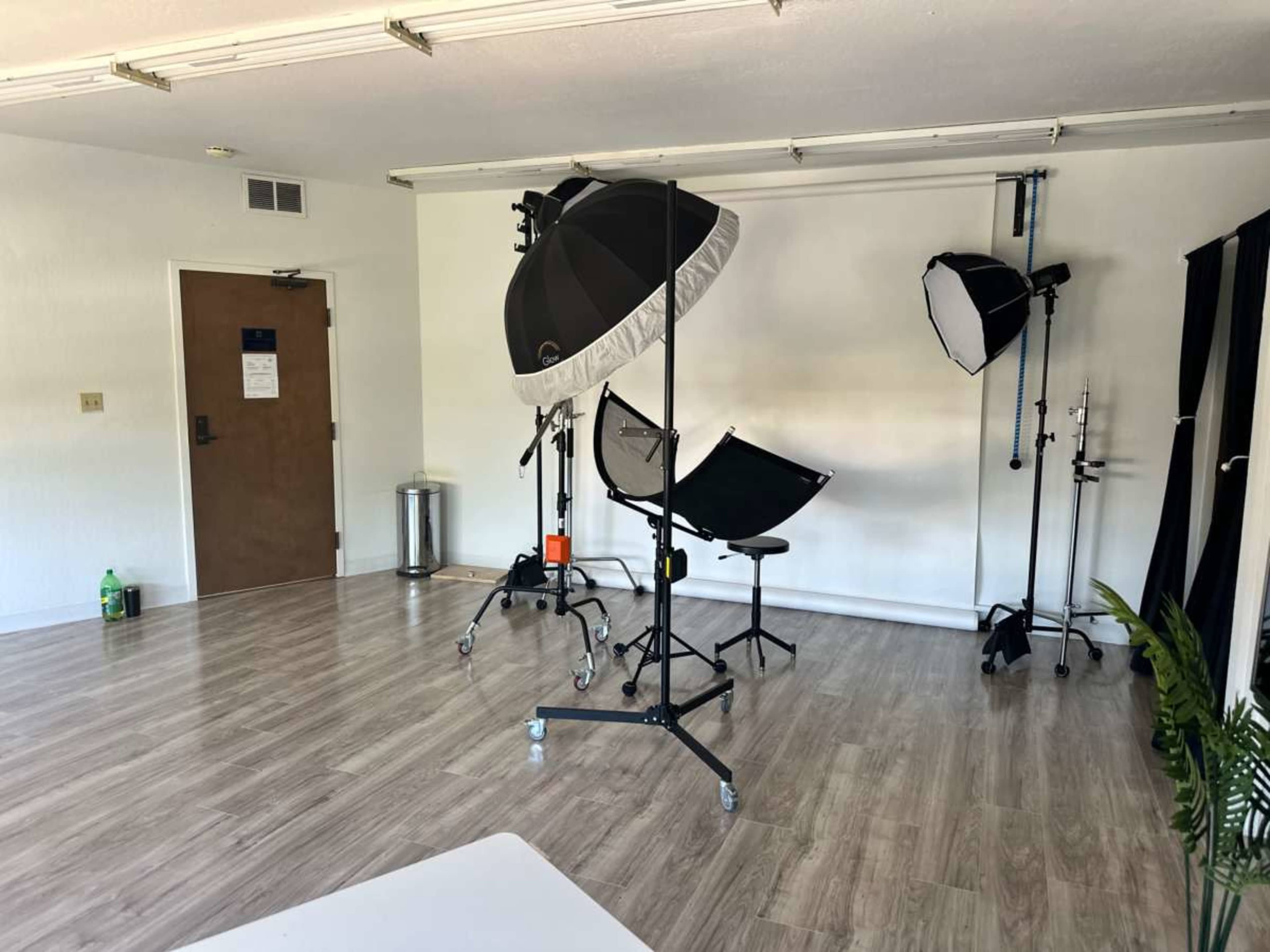 A photography studio equipped with light stands and backdrops, featuring a chair in the center and a door in the background.