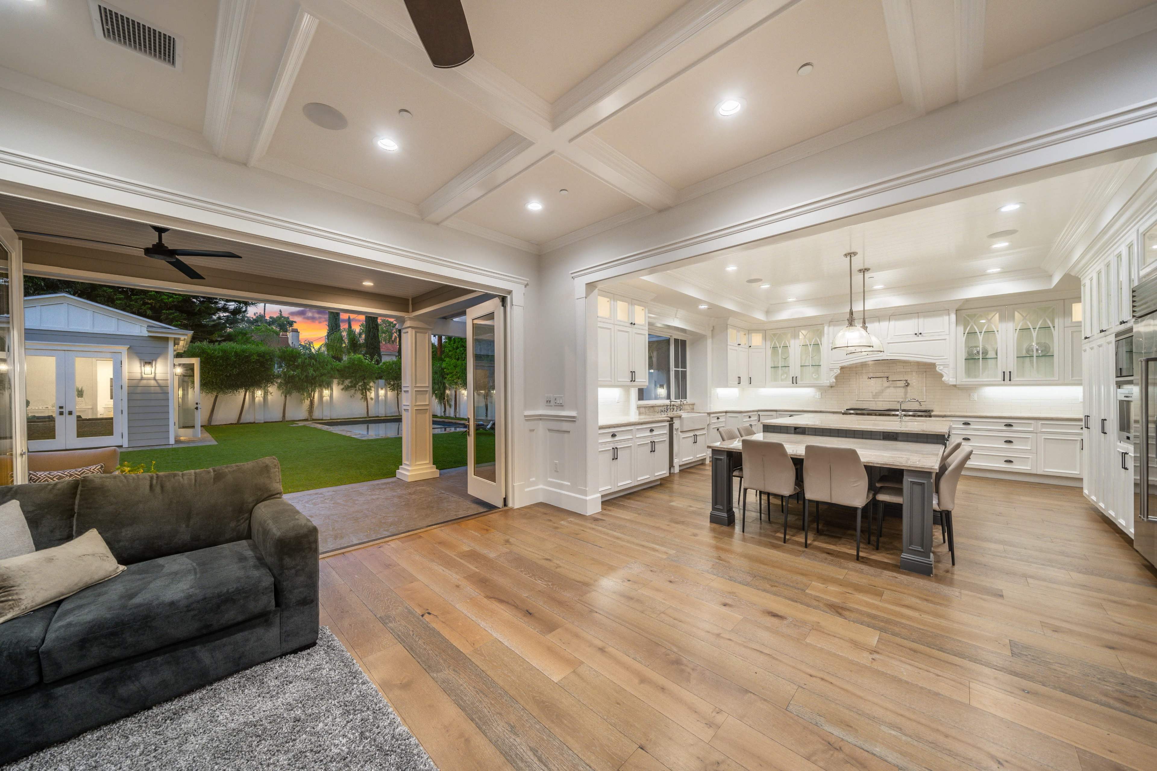 A spacious kitchen features white cabinetry and a large island, seamlessly connecting to an outdoor area with a lawn.