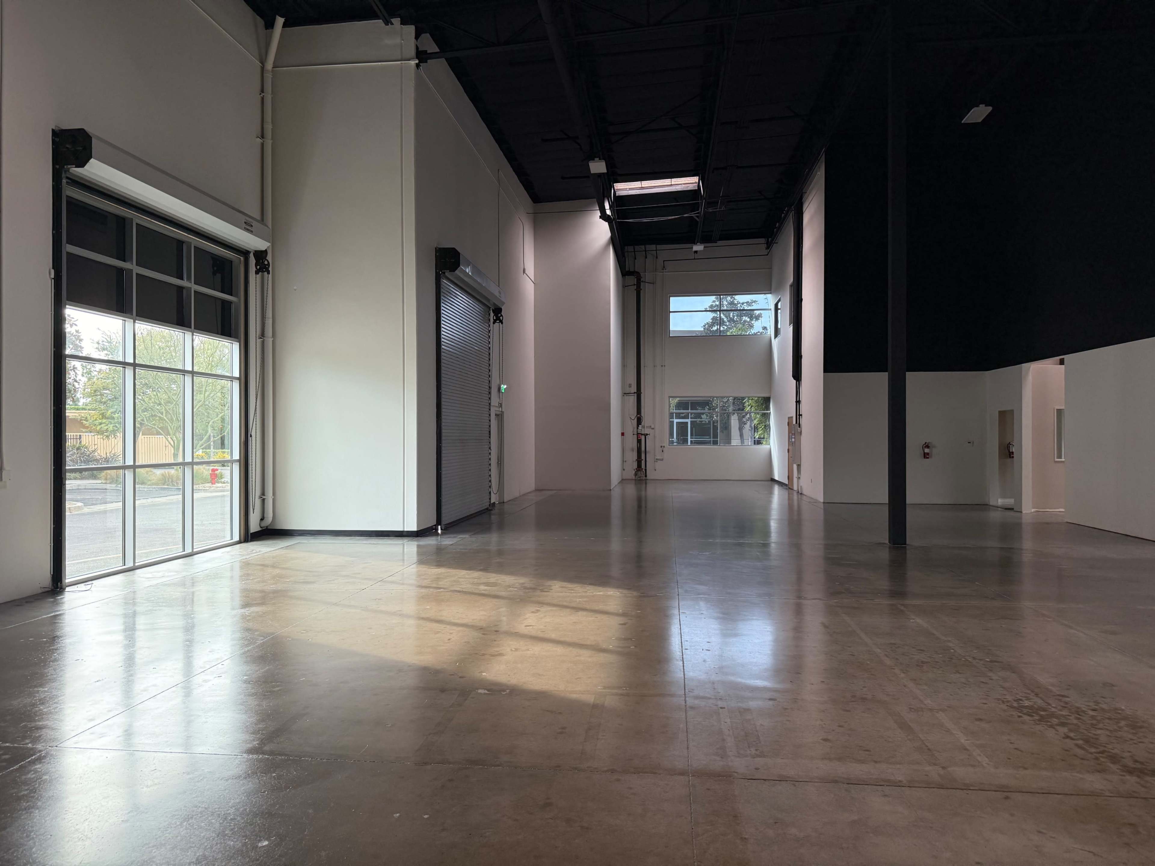 The image shows a large, empty industrial space with polished concrete floors and large windows allowing natural light to enter.