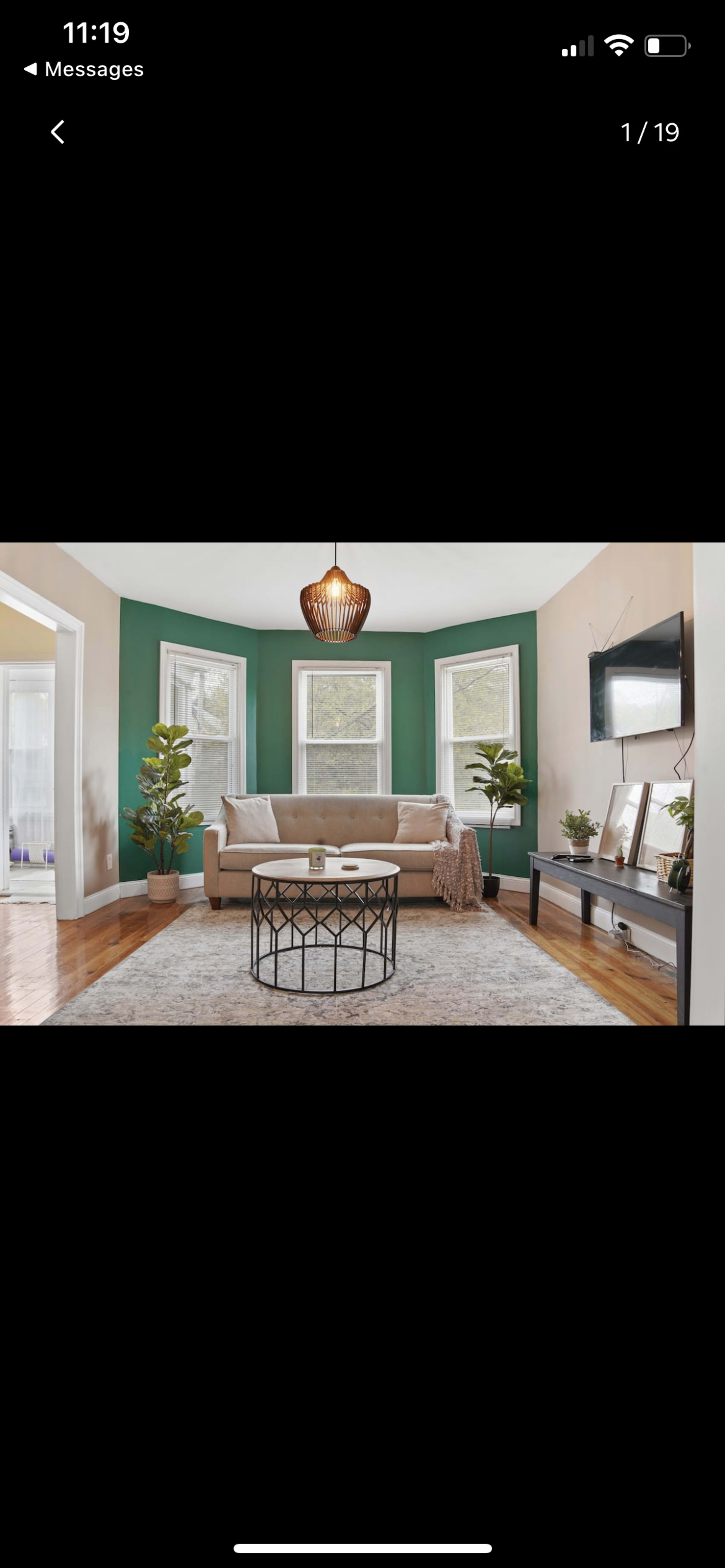 The living room features a beige couch, a round coffee table, green accent walls, and large windows that allow natural light to fill the space.
