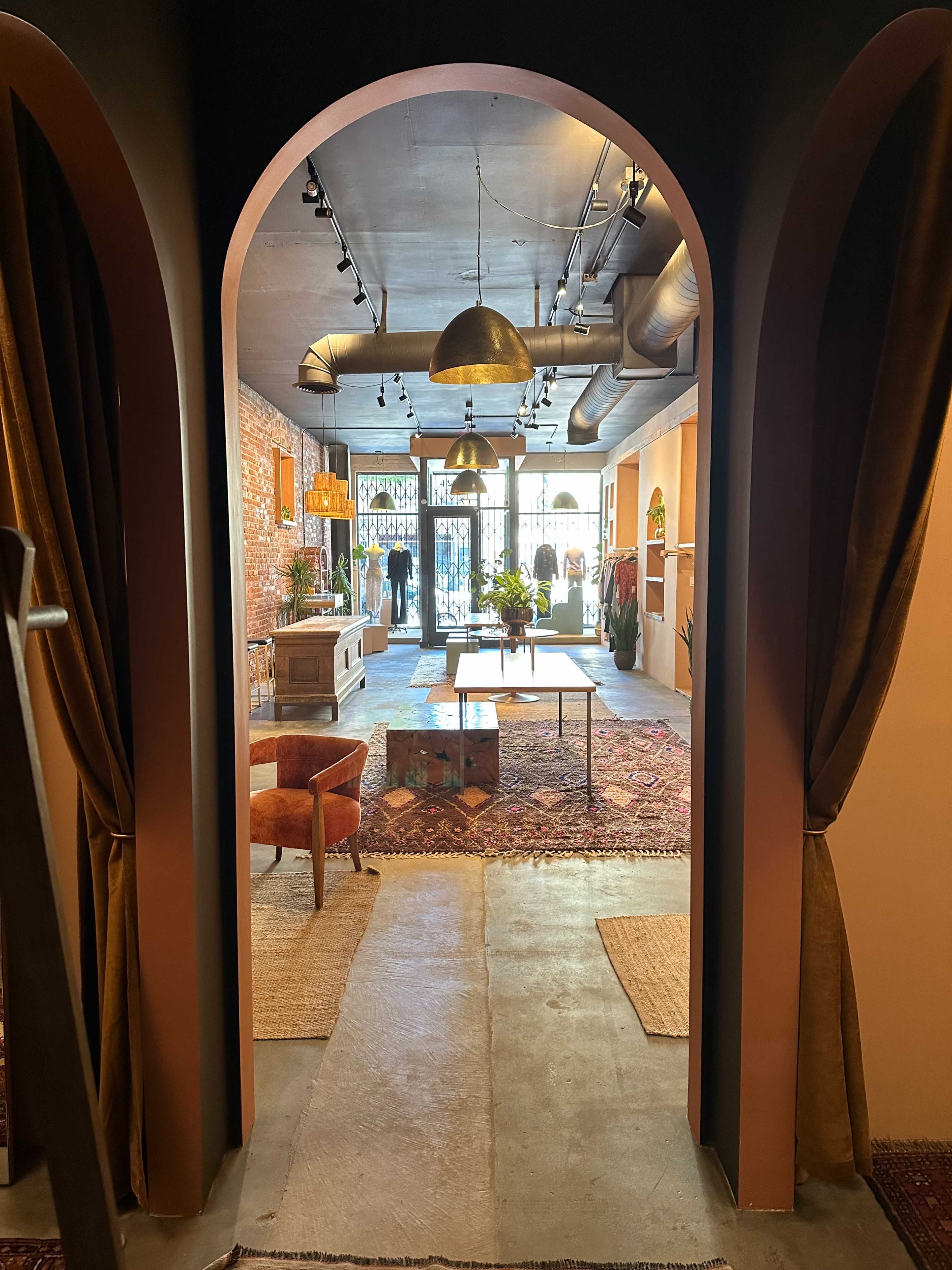 The image shows an interior space with arched doorways leading to a stylish room featuring seating, plants, and decorative elements on the walls and floor.